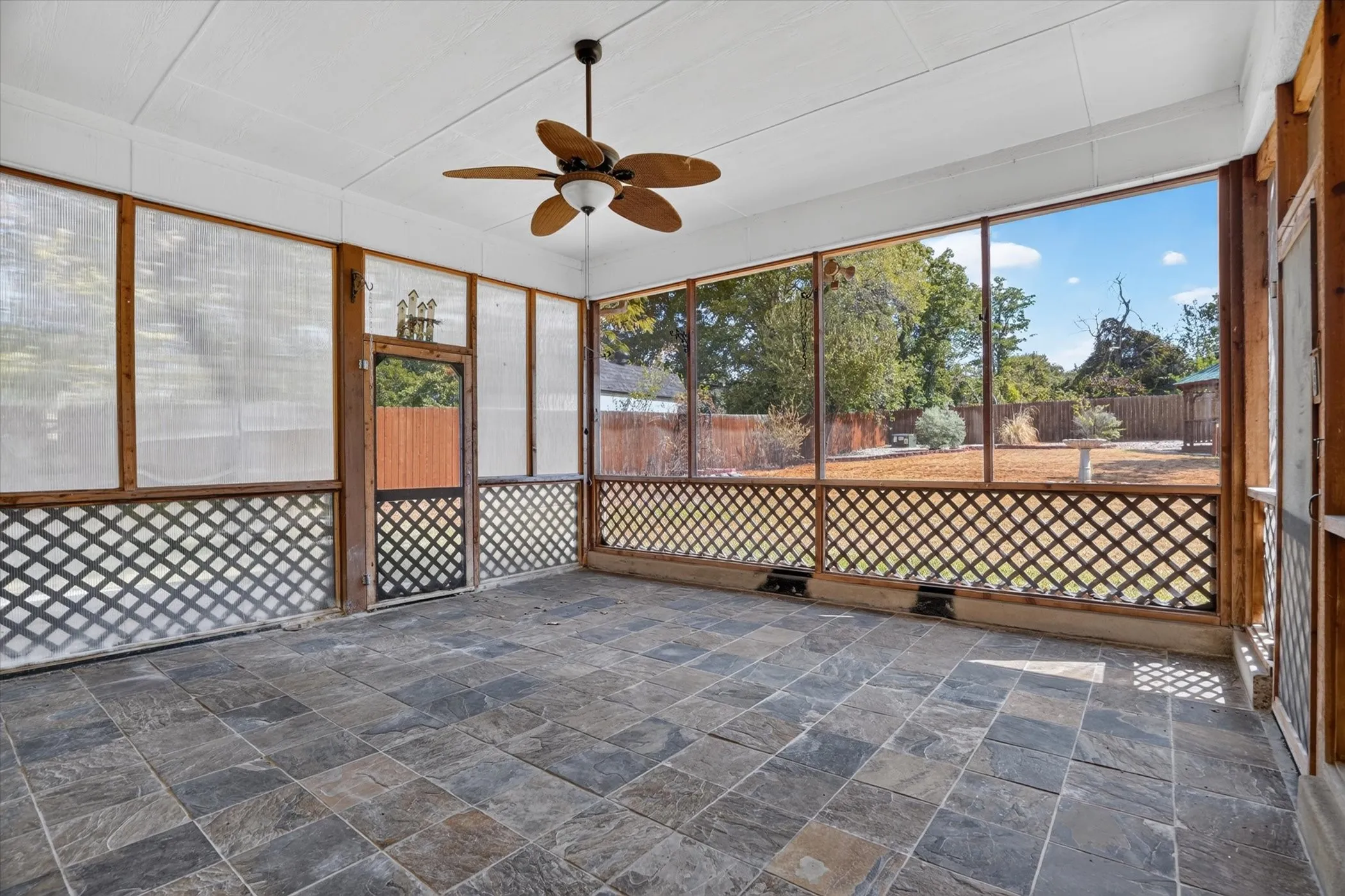 Spacious screened porch featuring a ceiling fan, slate tile flooring, and wood lattice detailing