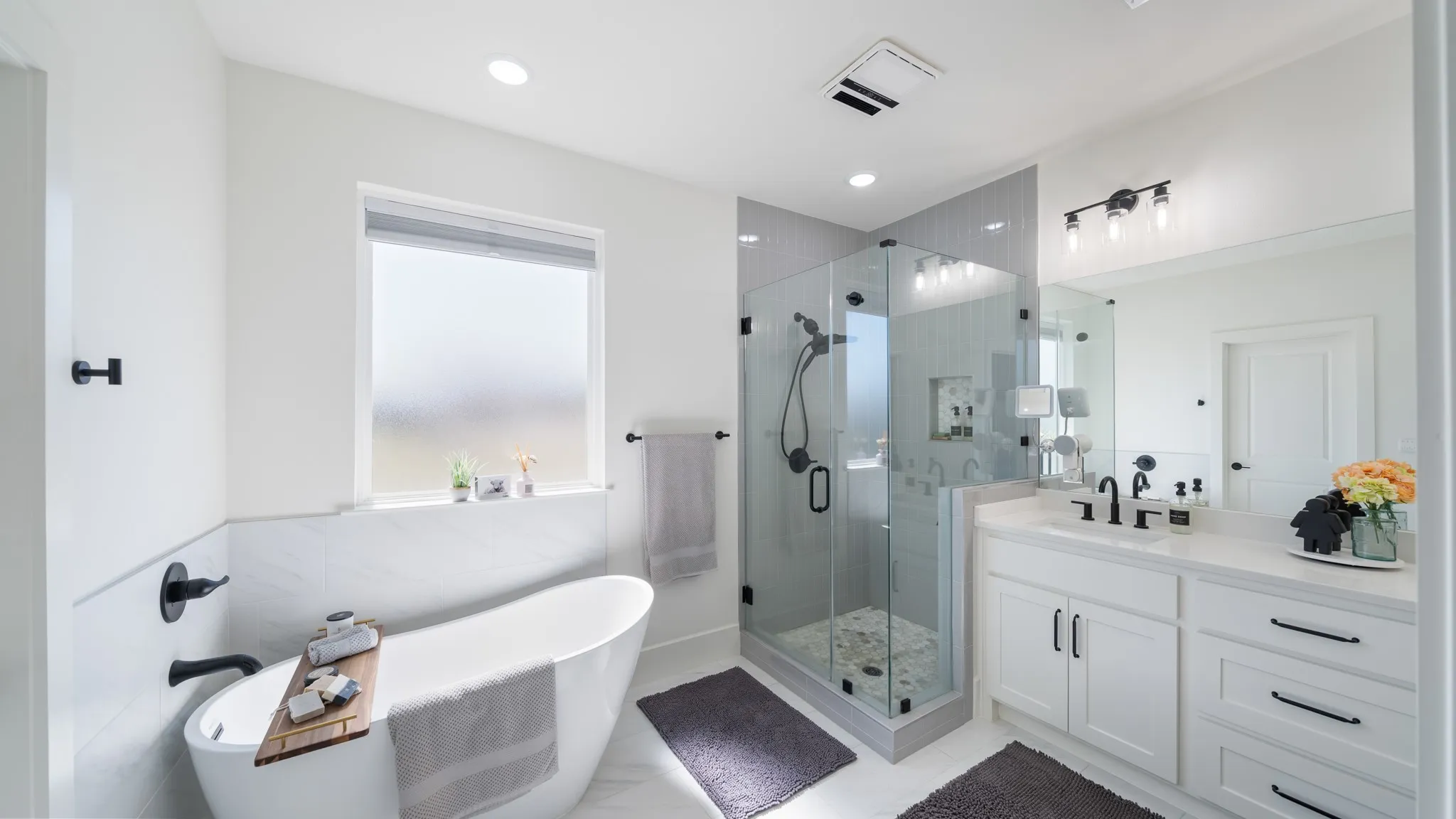 Freestanding soaking tub with black fixtures, glass-enclosed shower with tile surround, white vanity with stone countertop, and recessed lighting
