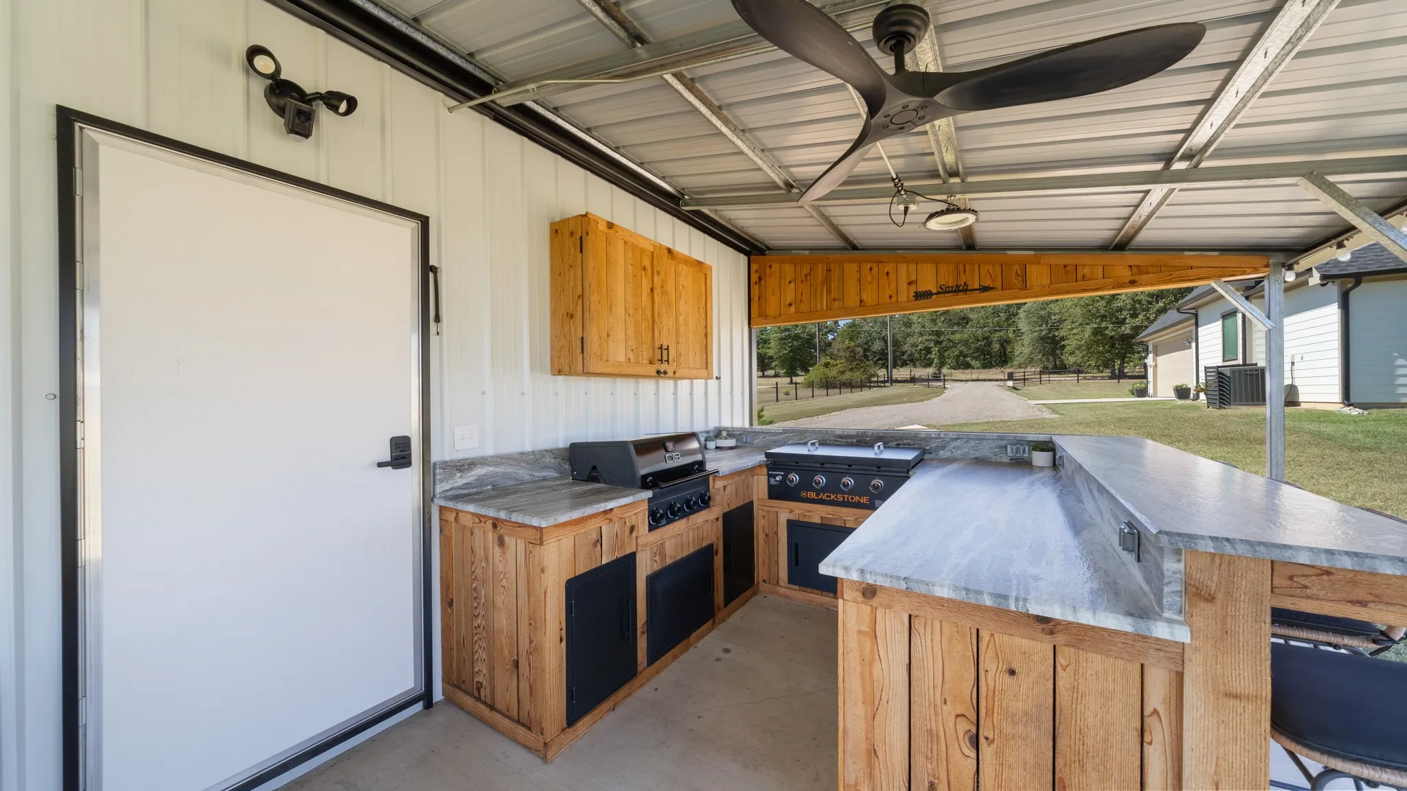 Outdoor kitchen featuring a built-in grill, sink, and bar-height counter, with wood-finish cabinetry and overhead lighting