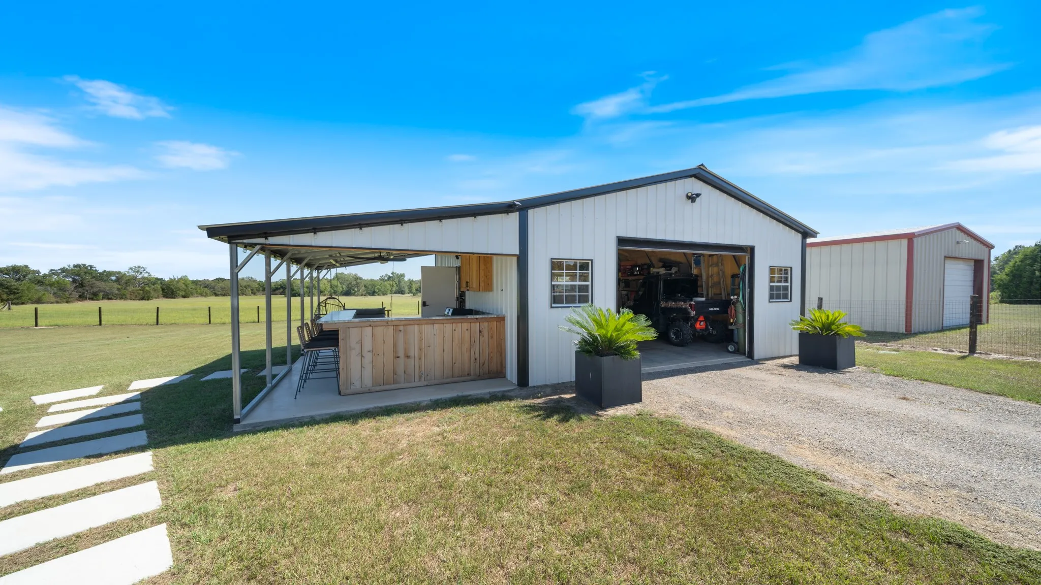 Detached garage with covered patio, built-in bar, wood-finish cabinetry, and gravel driveway