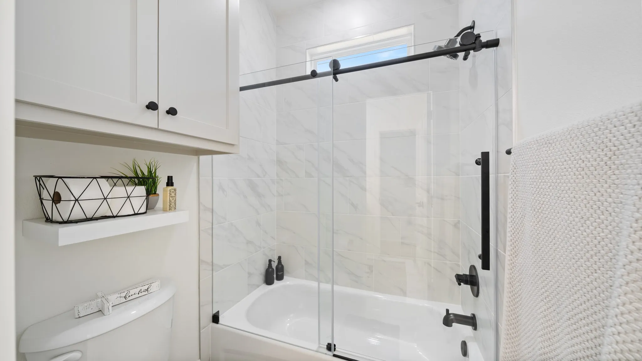 Spa-inspired primary bathroom featuring a frameless glass-enclosed shower with marble-look tile surround, white subway tile accents, and matte black hardware