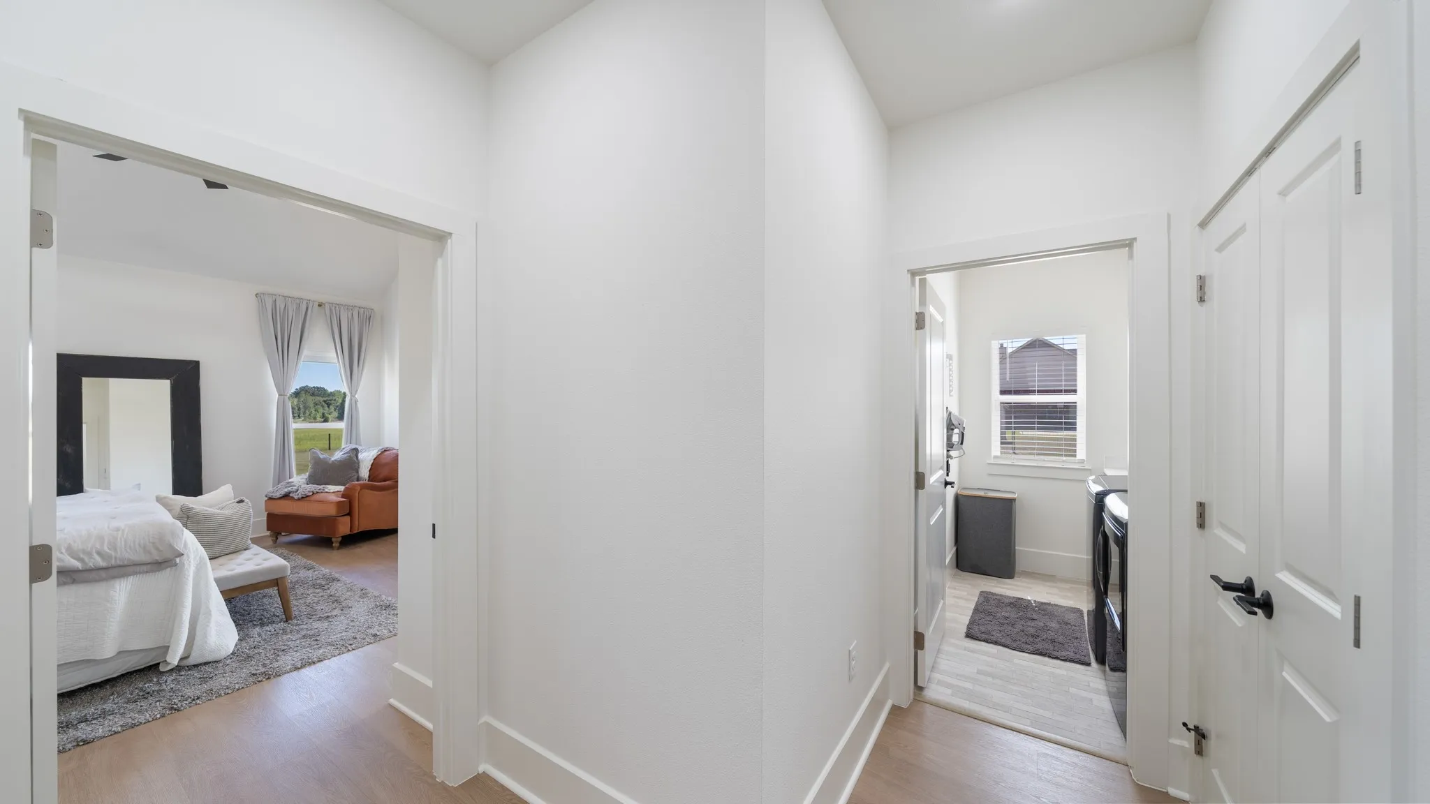 Bright hallway with white painted walls and wood-finish flooring, featuring multiple white interior doors with brushed nickel hardware and transom windows that allow natural light throughout the space
