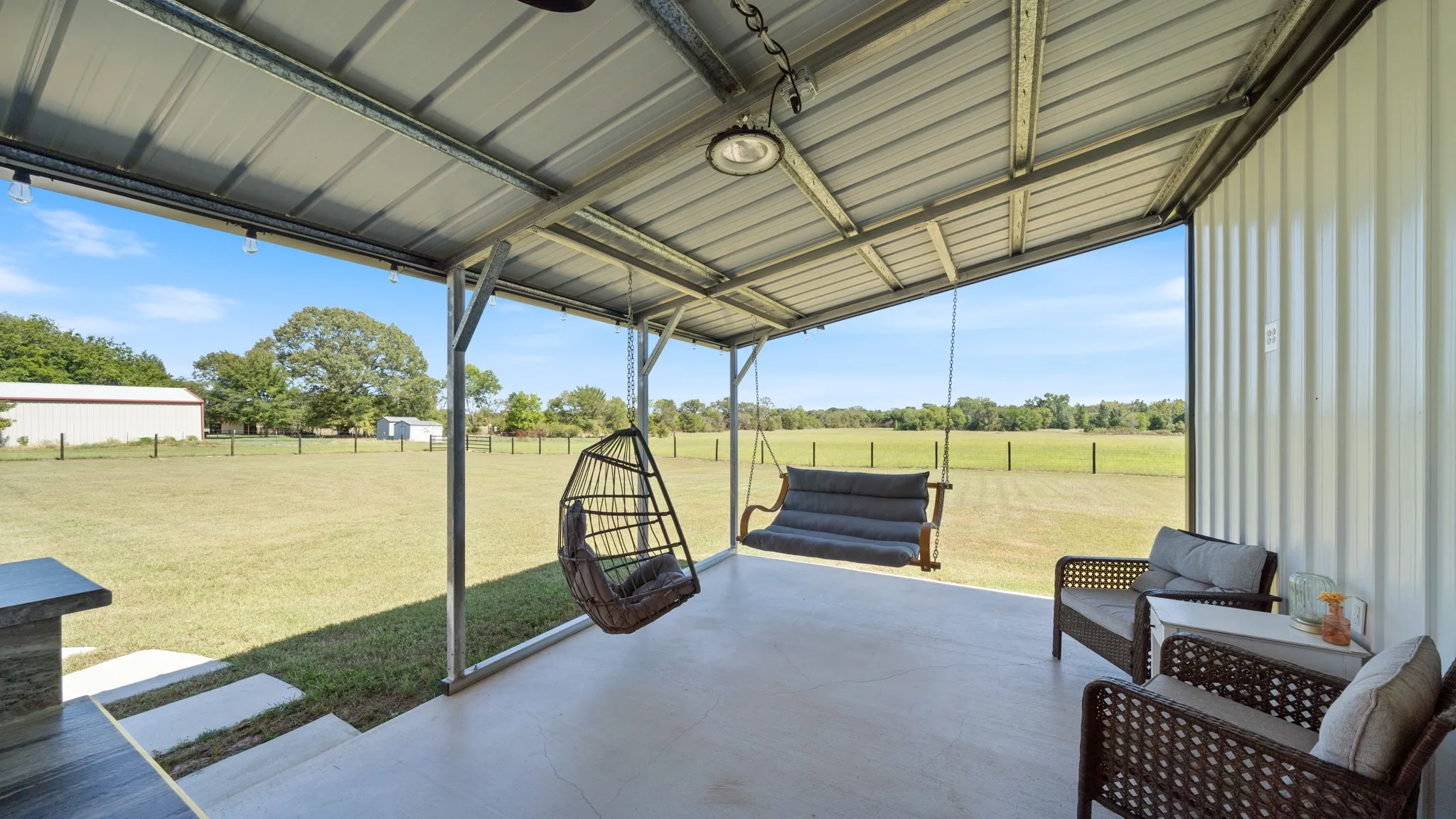 Covered patio with polished concrete flooring and steel-frame pergola roof structure, overlooking expansive pastureland