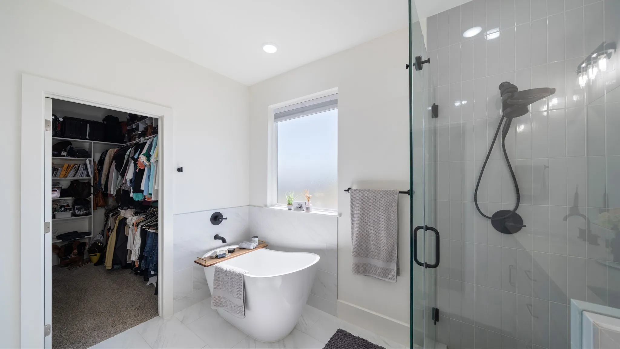Spa-inspired primary bathroom featuring a freestanding soaking tub, walk-in shower with subway tile surround and rainfall showerhead, floating vanity with vessel sink, heated towel rack, and abundant natural light from corner window