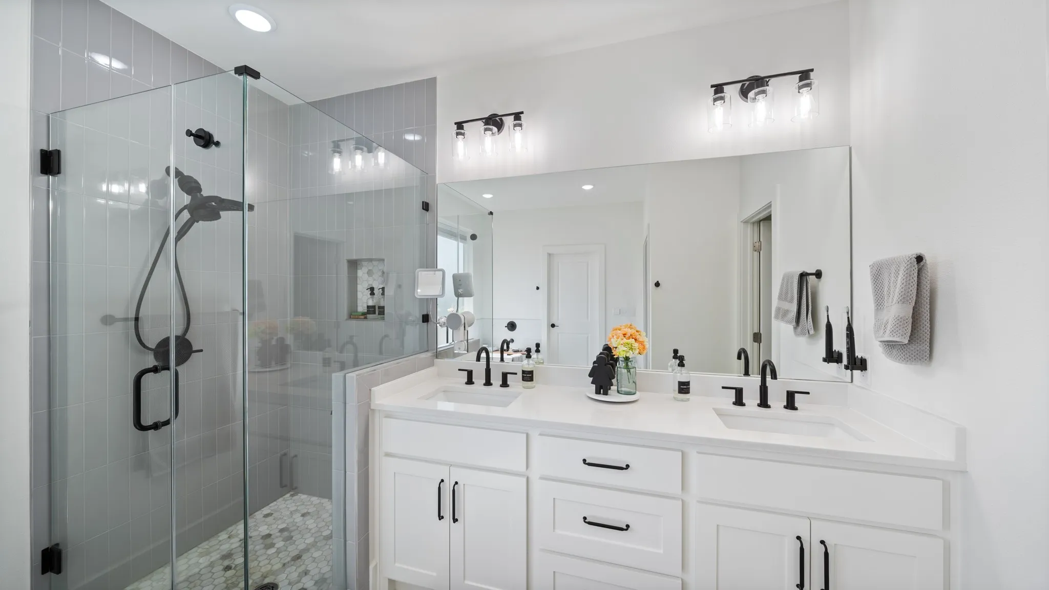 Dual vanity with white cabinetry, matte black hardware, and an expansive mirror