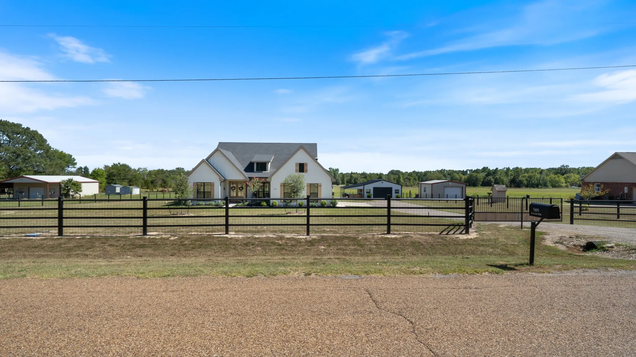 White exterior with dark roof, fenced perimeter, and detached structures