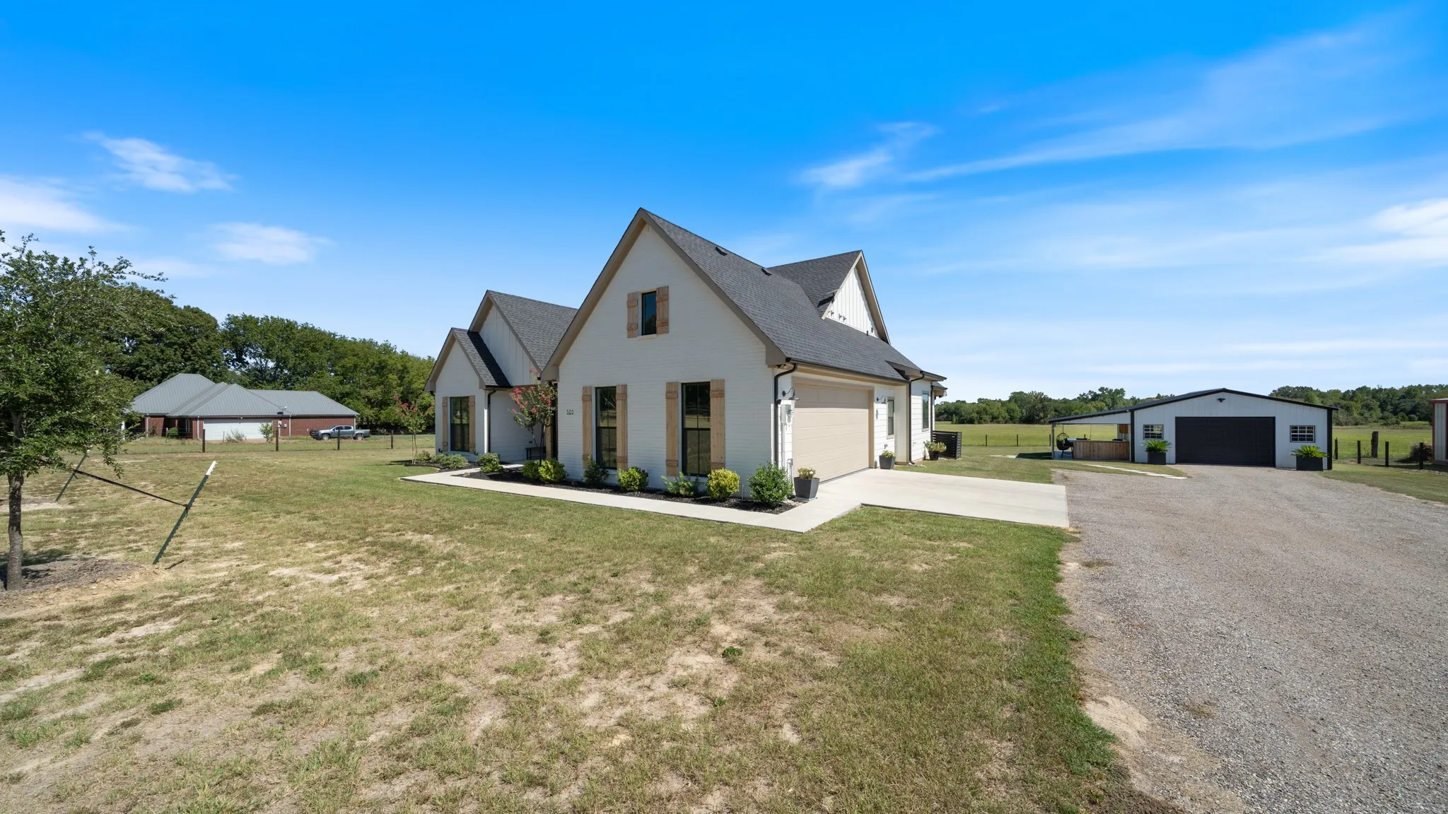 Modern farmhouse residence showcasing a steeply pitched gabled roof with dark asphalt shingles, light-colored exterior cladding, and multi-pane windows