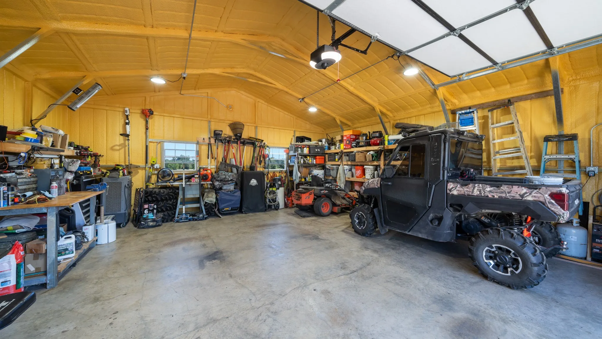 Spacious interior with high ceilings, exposed beams, ample task lighting, two windows, and concrete flooring