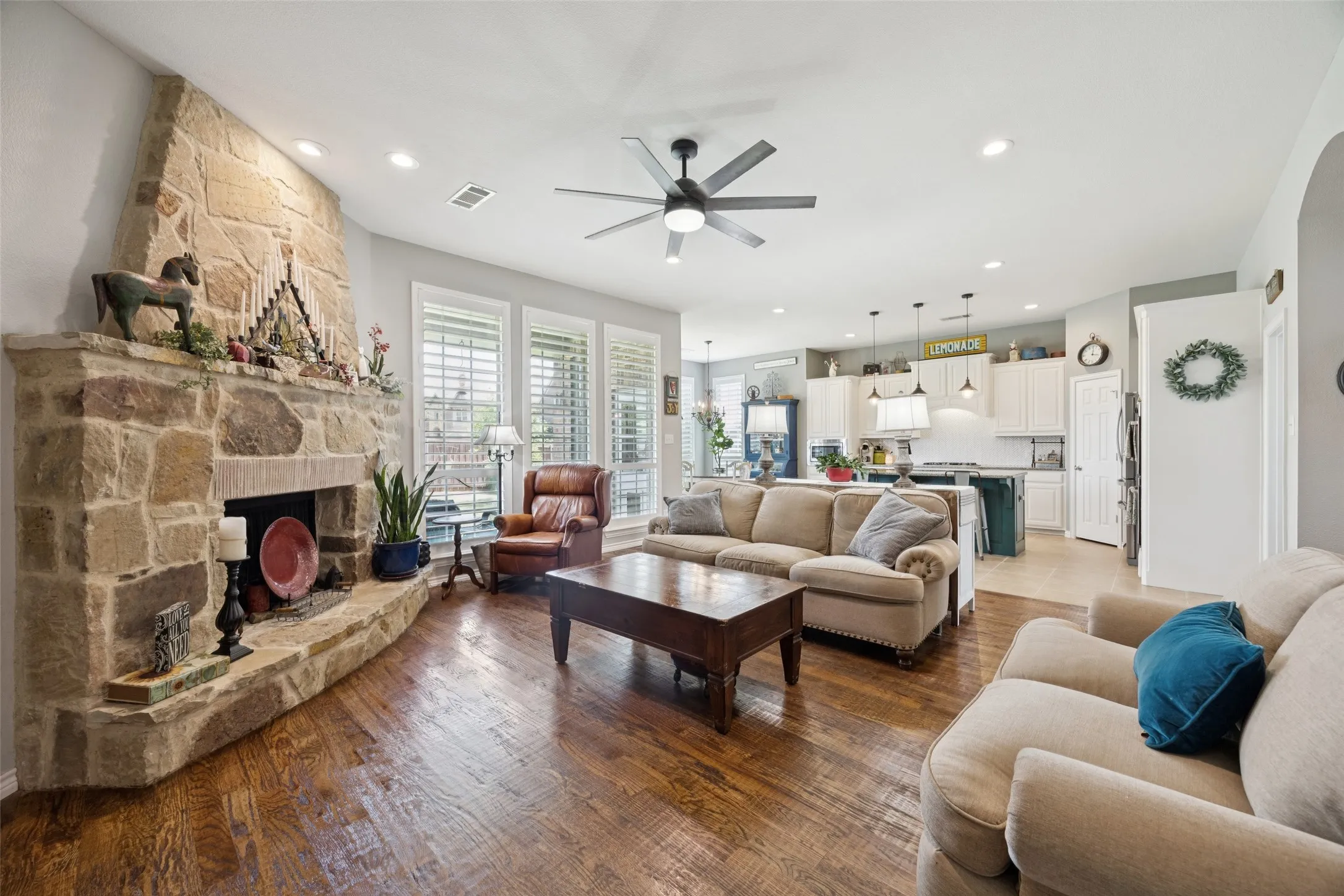 Stone fireplace, wood-finish flooring, recessed lighting, ceiling fan, and white plantation shutters