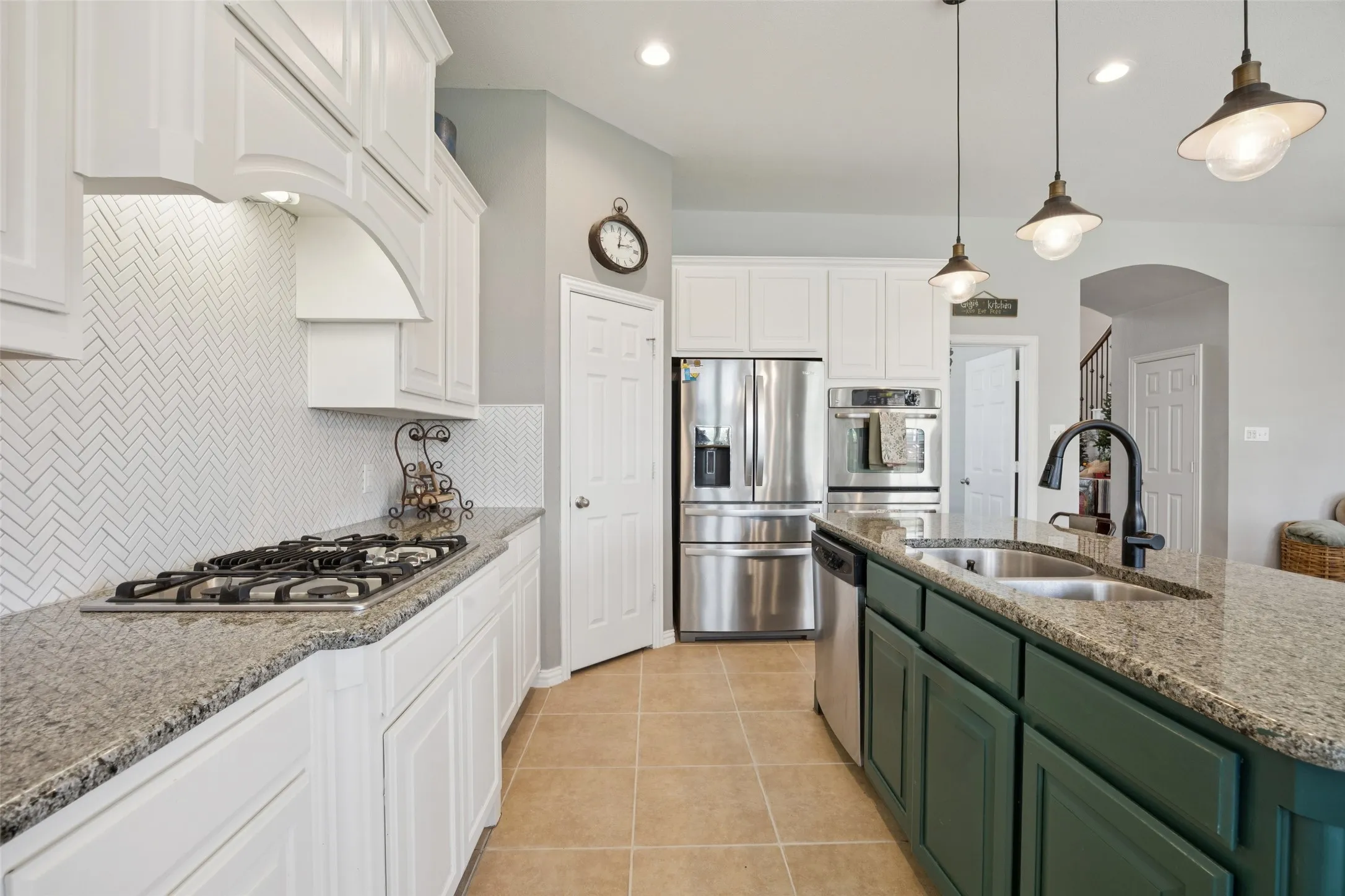Kitchen featuring white shaker-style cabinetry, a herringbone pattern tile backsplash, a built-in gas cooktop, stainless steel appliances, and a central island with a double basin sink