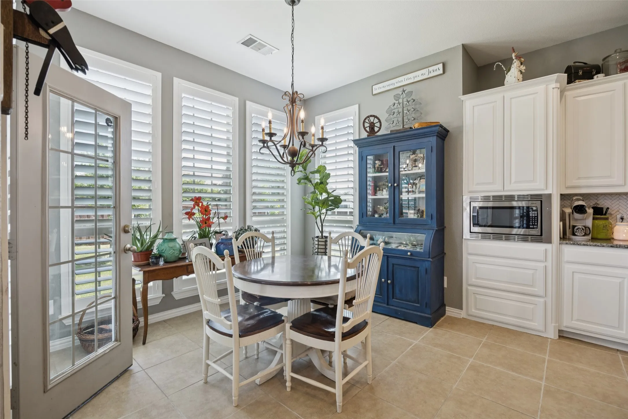 Tile flooring, white cabinetry, built-in microwave, chandelier lighting, and shuttered windows
