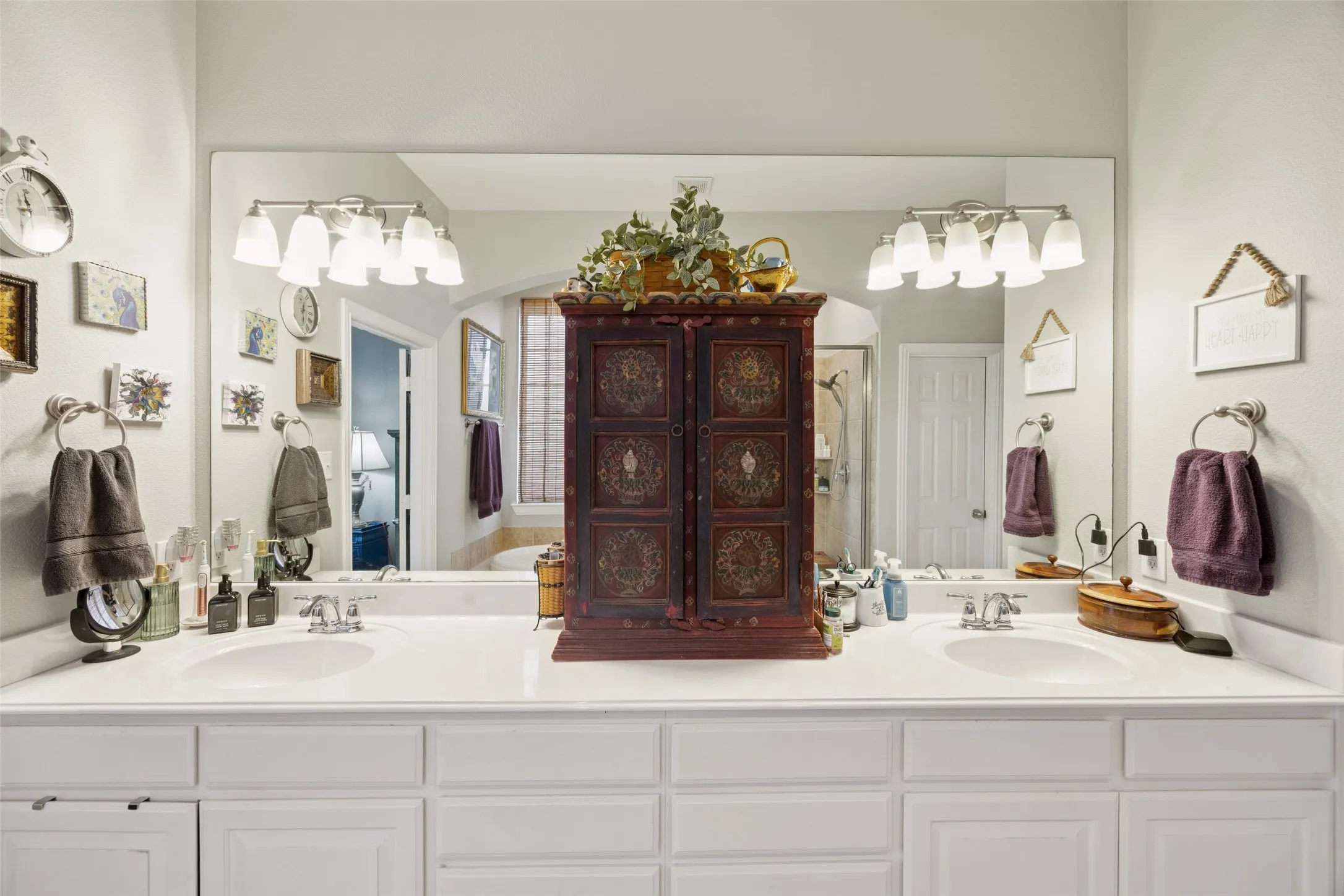 Dual undermount sinks, white countertop, extensive vanity mirror, wall-mounted light fixtures, and white cabinetry