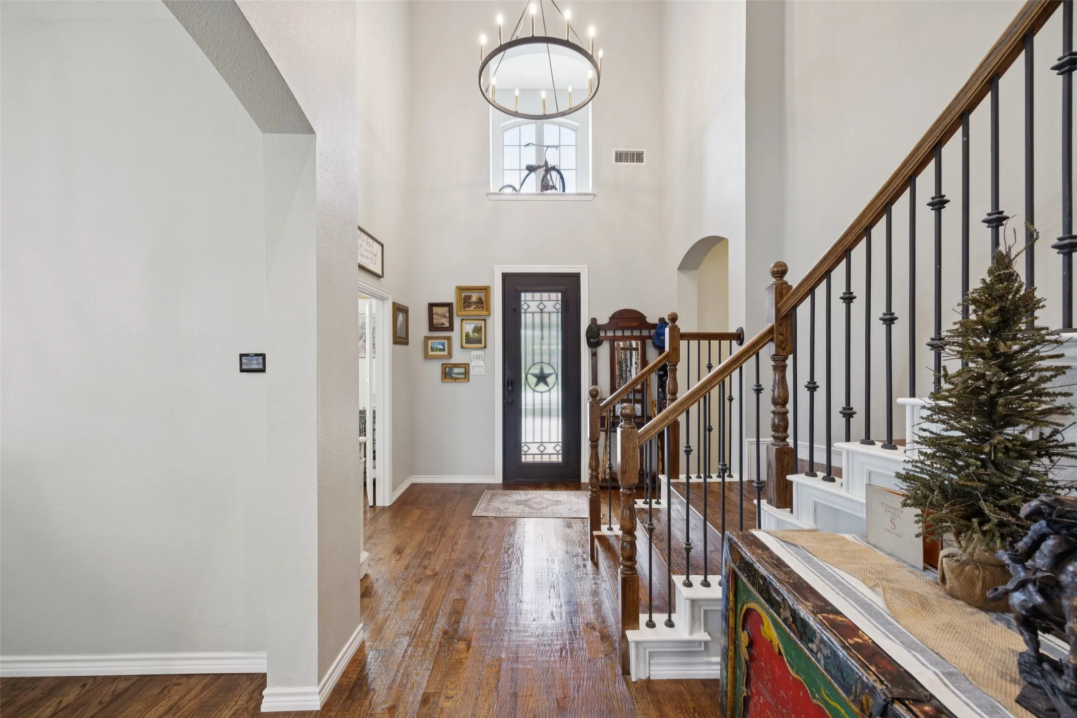 Soaring ceilings with a large chandelier, wood-finish flooring, and a staircase with dark wood handrails and wrought iron balusters