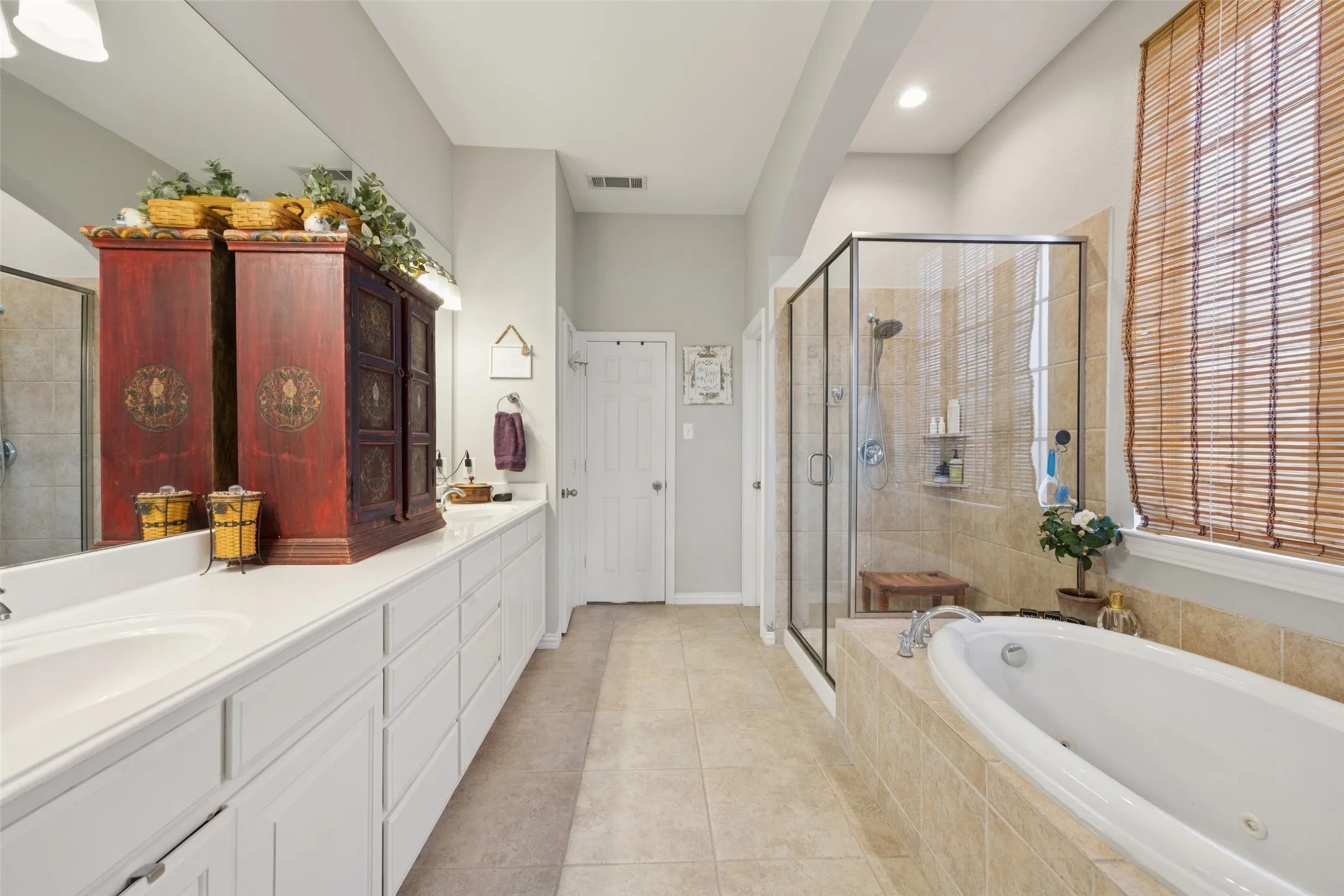 Dual vanity with extensive white cabinetry, large built-in soaking tub, separate glass-enclosed shower, and tiled flooring