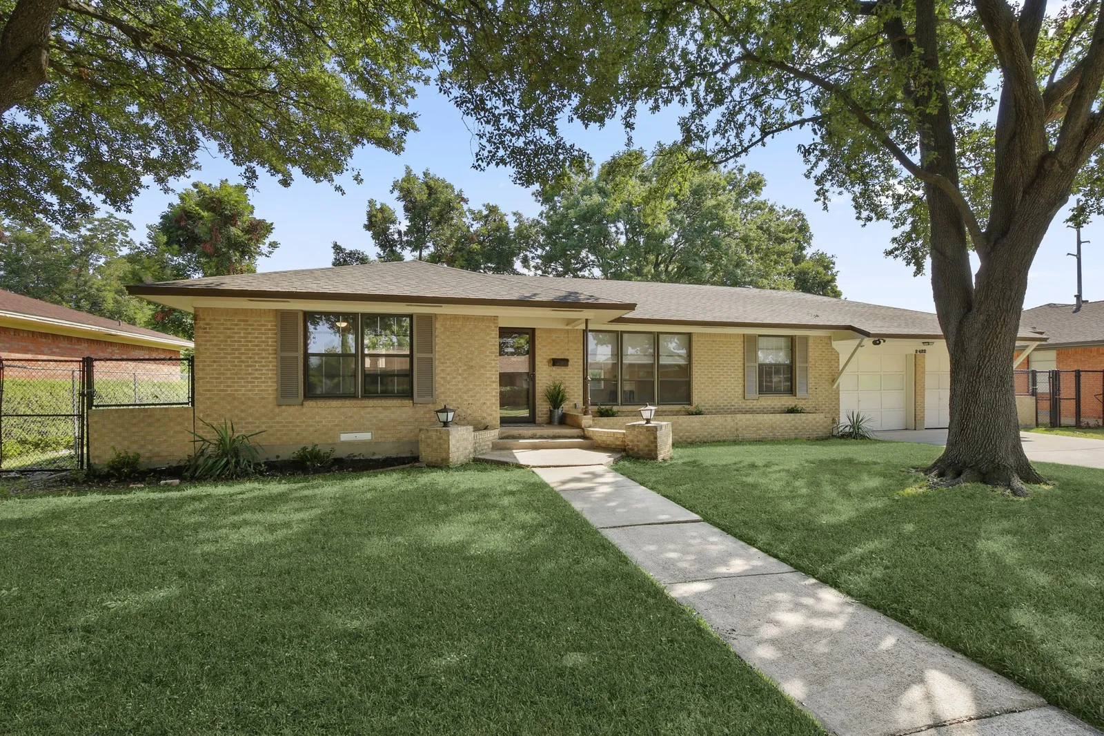 Single-story brick exterior with a low-pitch roof, an attached garage, and a concrete pathway leading to the entry