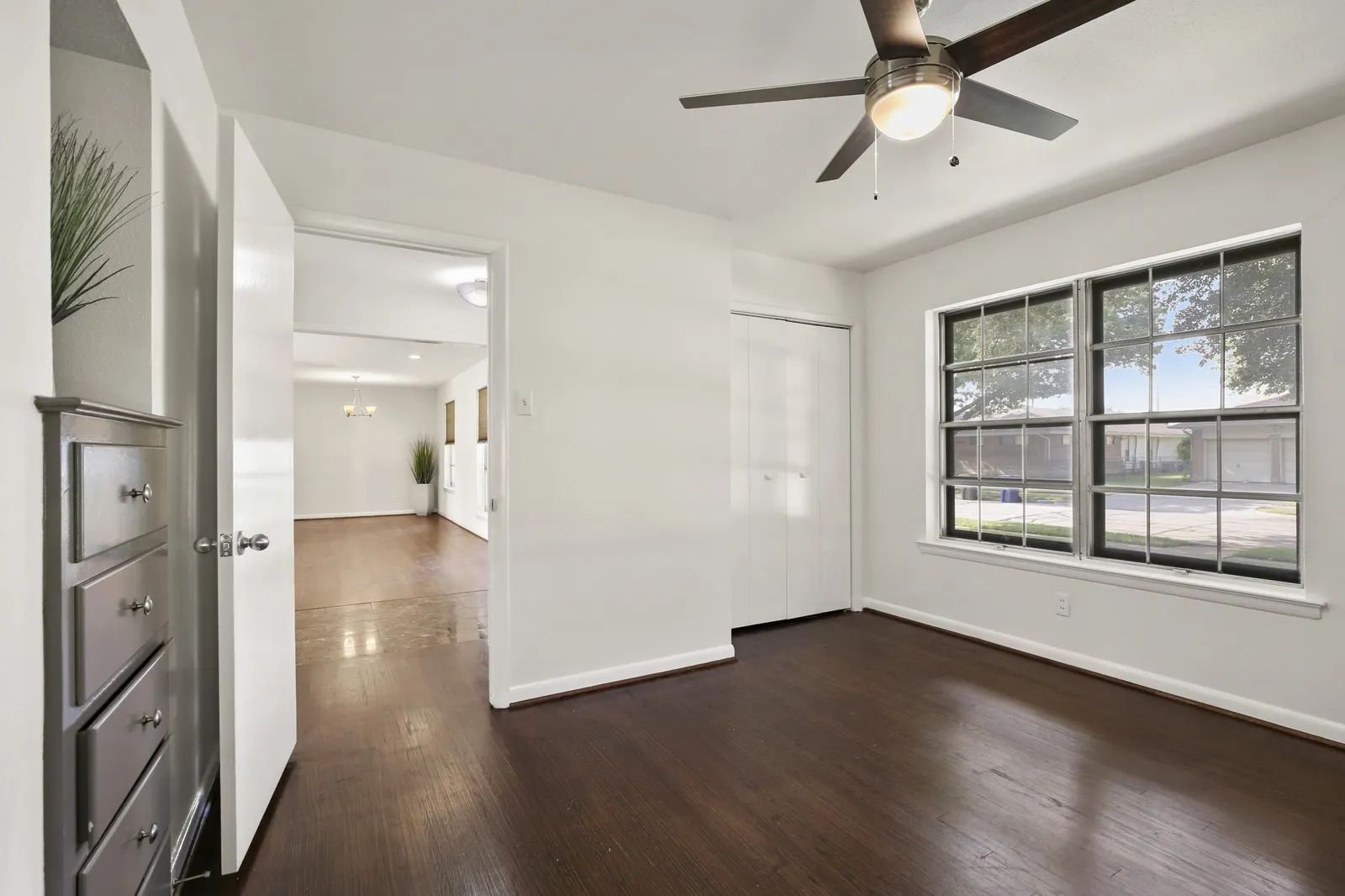 Hardwood flooring, crisp white walls, contemporary ceiling fan with integrated lighting, bi-fold closet doors, and large grid-pattern windows