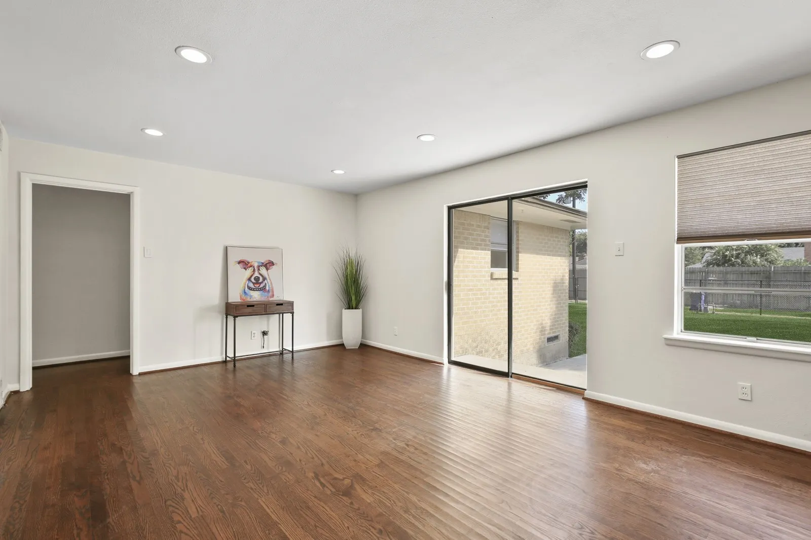 Recessed lighting illuminates the wood-finish flooring, complemented by a sliding glass door and a large window with privacy blinds