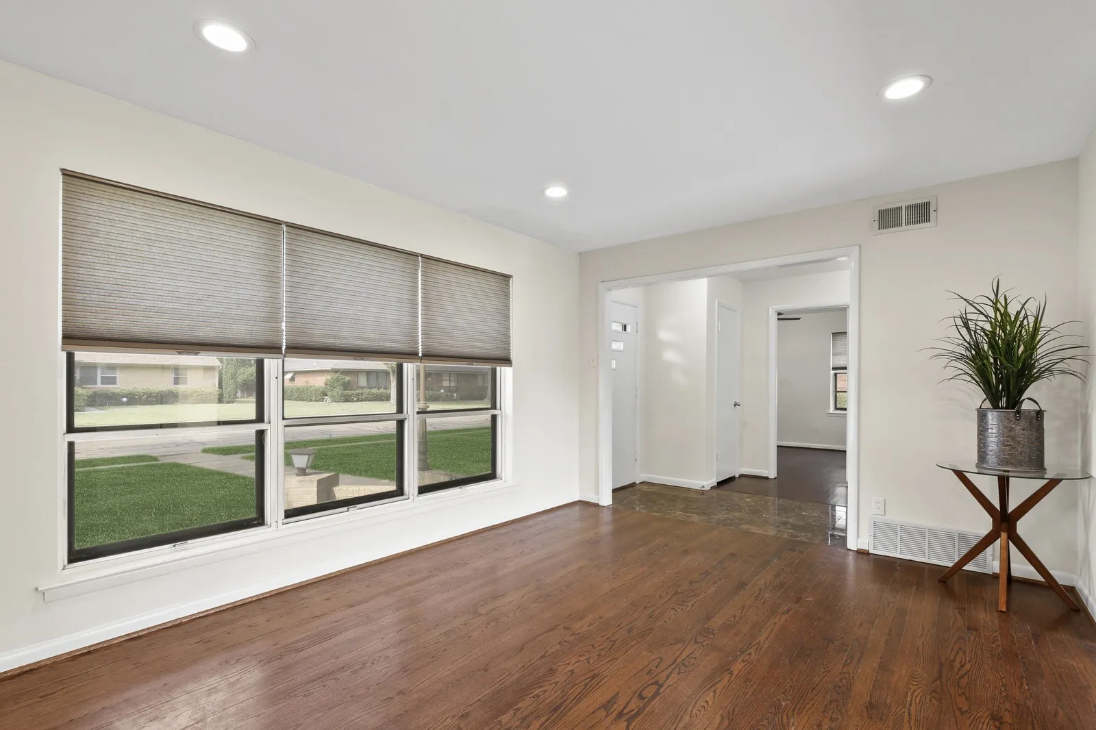 Rich wood-finish flooring, recessed ceiling lighting, bright window with blinds, and white interior walls