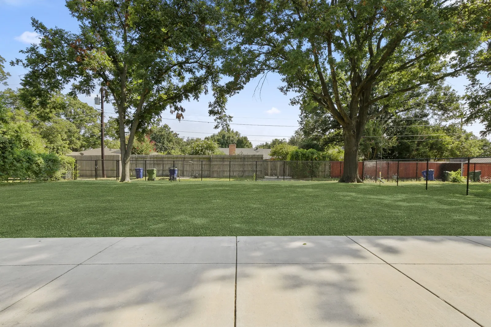 Expansive backyard featuring a manicured lawn, concrete patio, and mature trees
