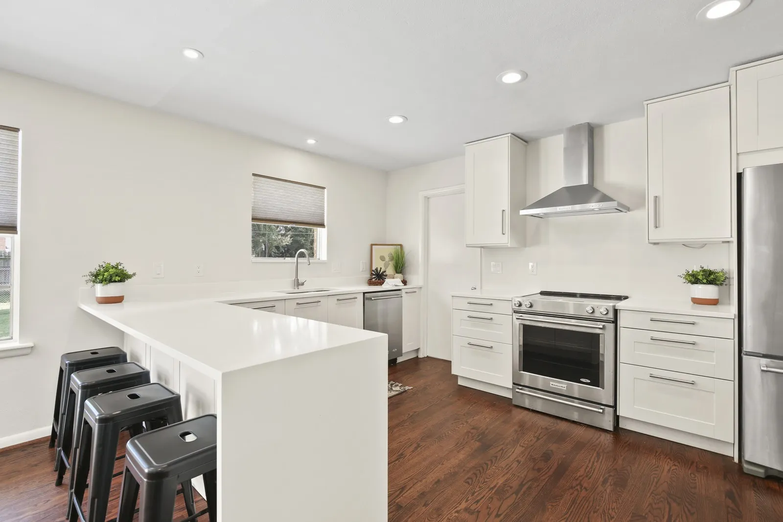 Kitchen featuring a breakfast bar with seating, white shaker-style cabinetry, stainless steel appliances, recessed lighting, and wood-finish flooring