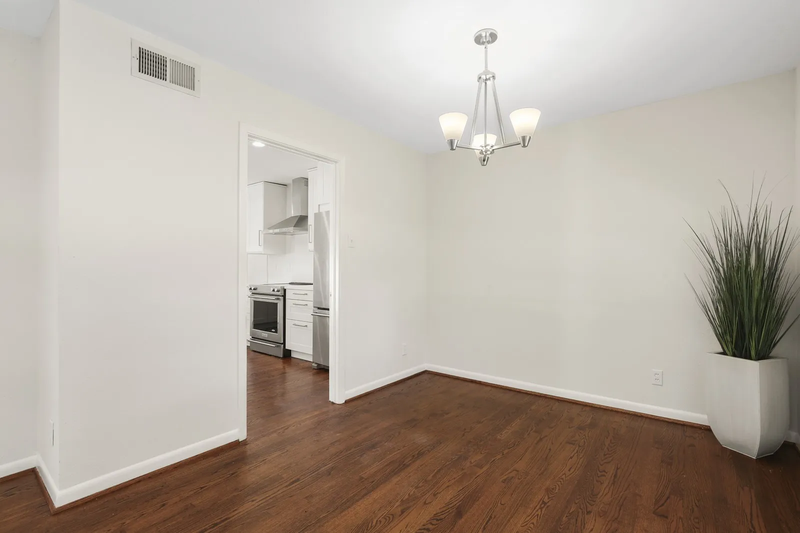 Hardwood flooring, contemporary chandelier, crisp white walls, and a recessed kitchen entry
