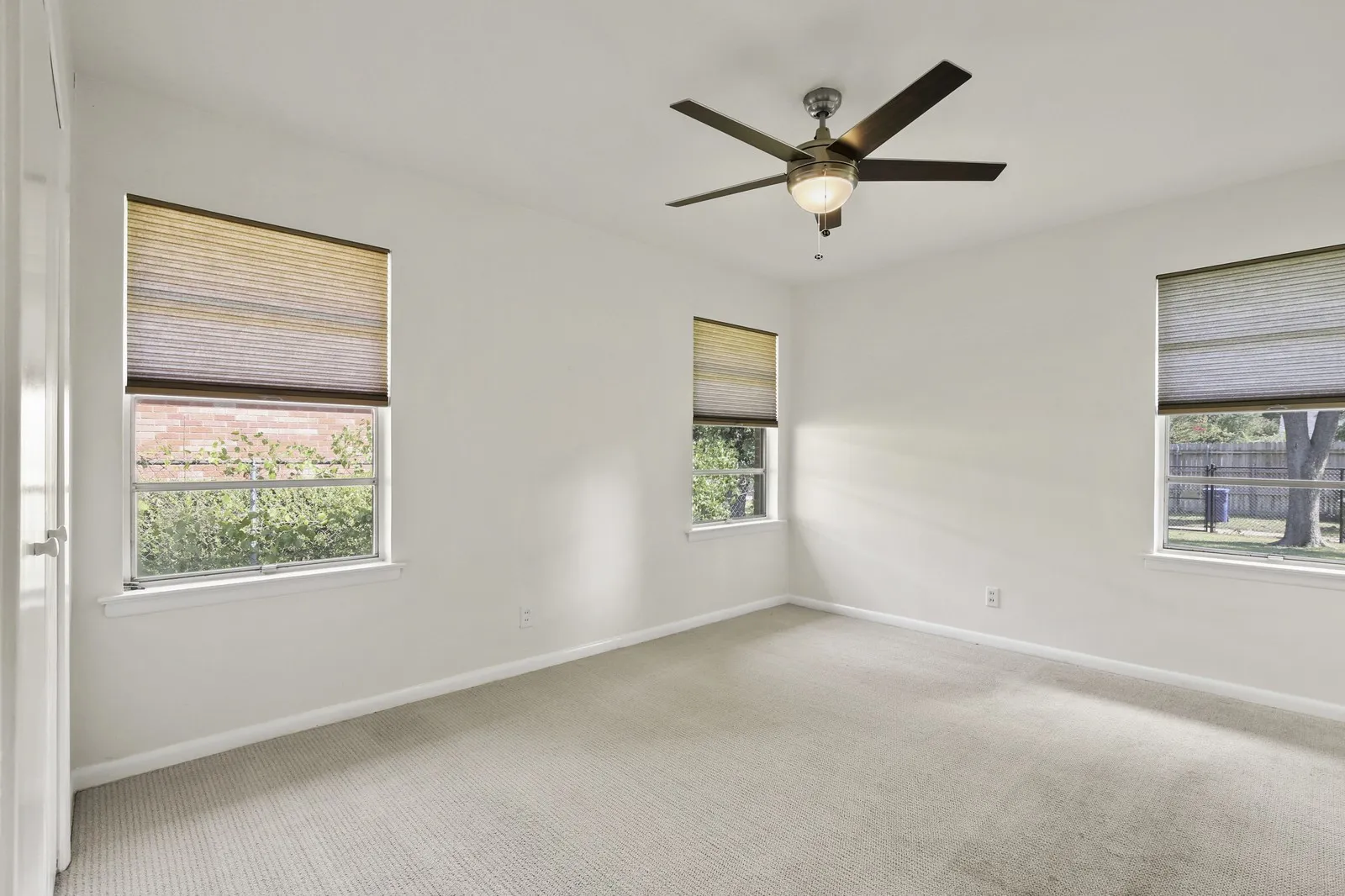 Neutral wall paint, three windows with cellular shades, ceiling fan with integrated lighting, and carpeted flooring