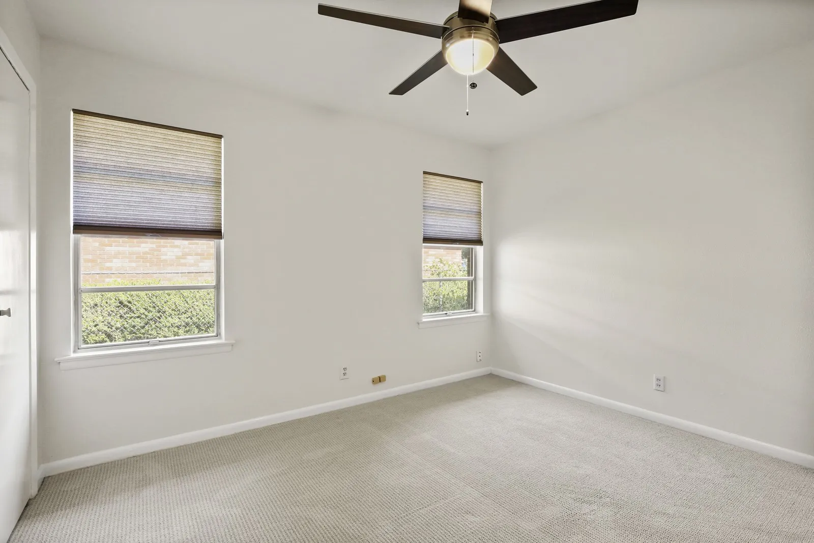 Neutral wall paint, textured carpet, two windows with blinds, ceiling fan with light fixture