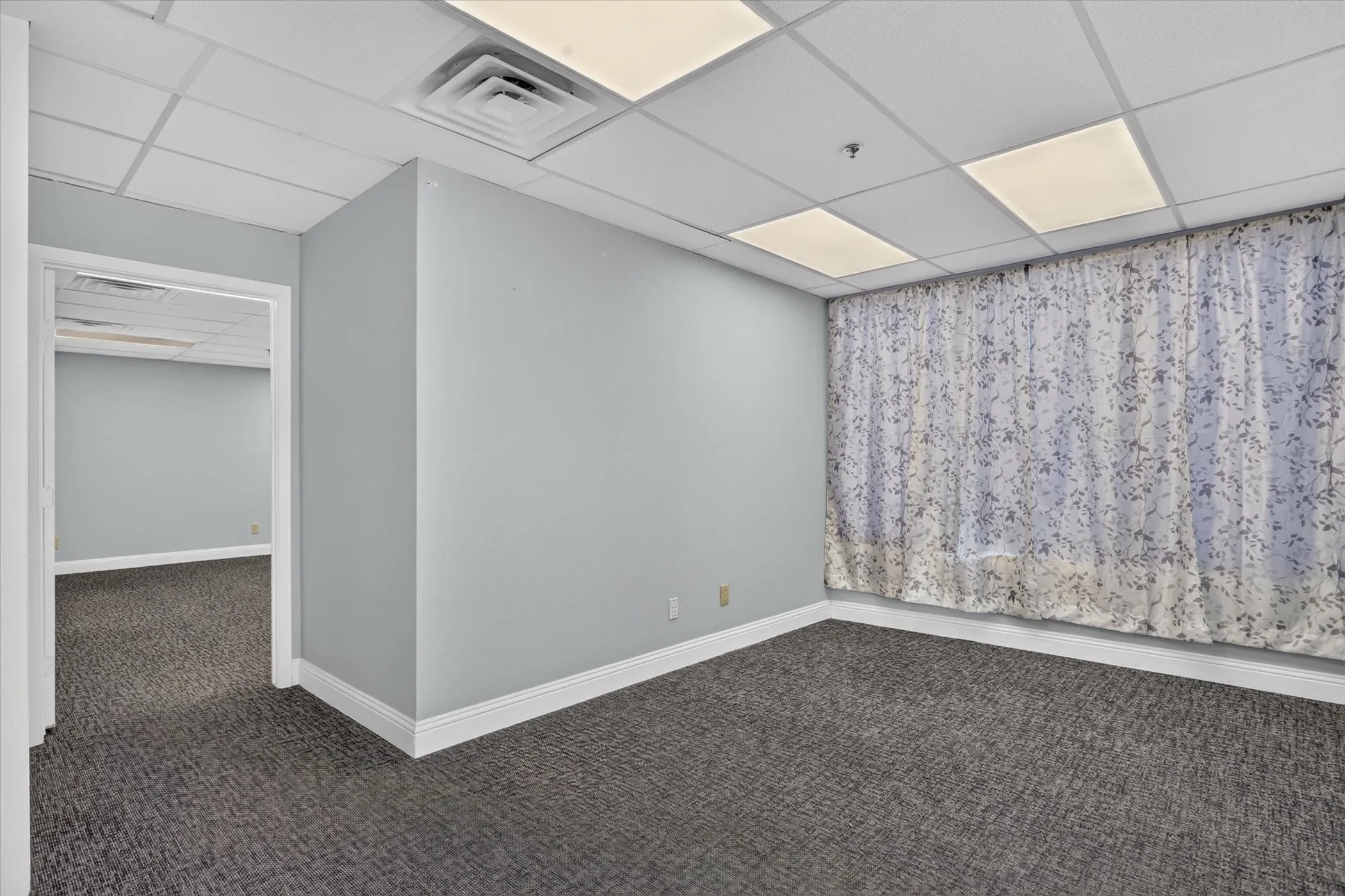 Recessed ceiling lighting, dropped ceiling panels, light gray wall paint, dark patterned carpeting, and white baseboards