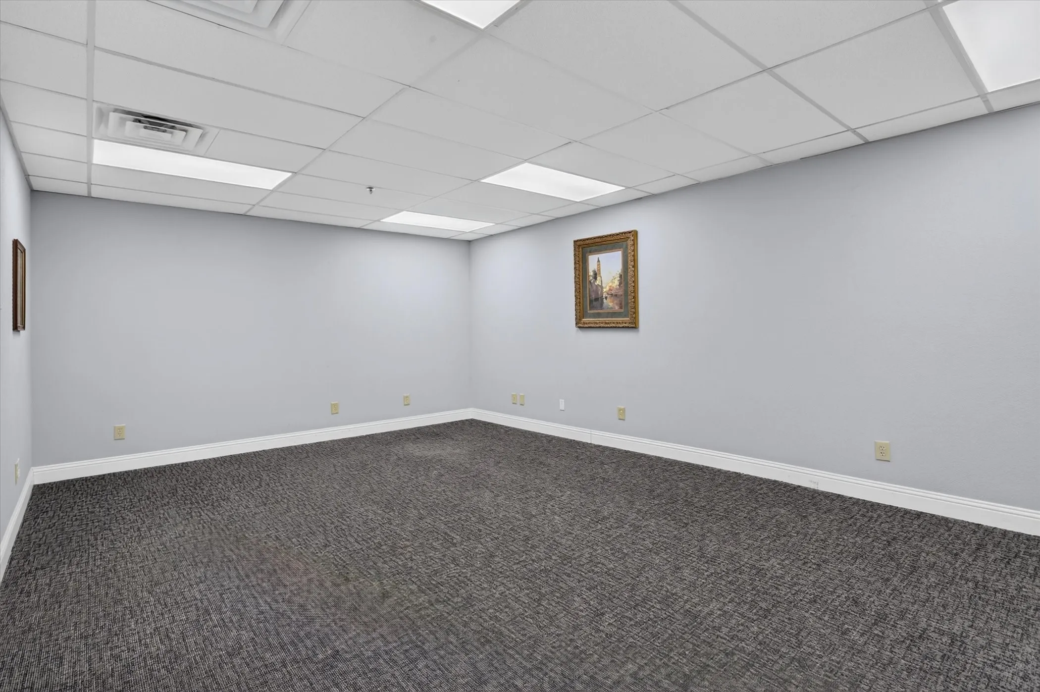 Recessed ceiling lighting, dropped ceiling grid, and gray walls, with patterned carpet flooring