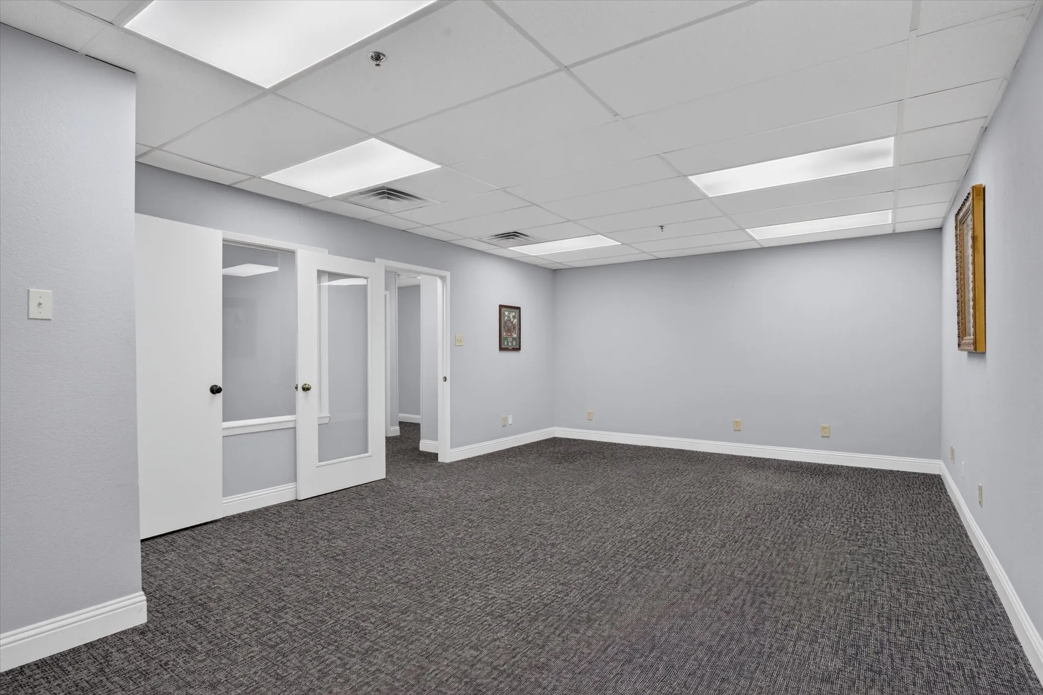 Expansive room with neutral carpeting, light gray wall finishes, and a grid ceiling with integrated lighting