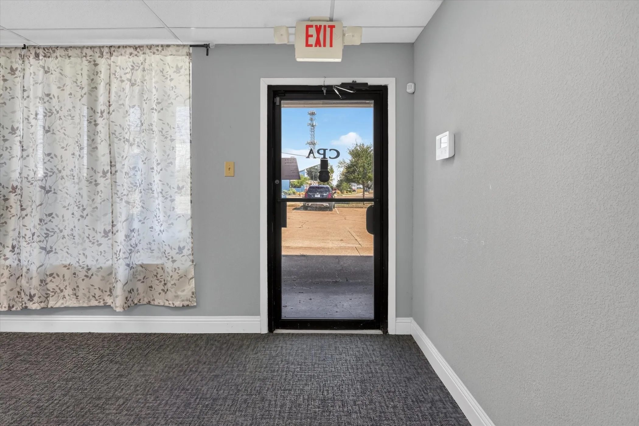 Glass-paneled entry door, textured grey walls, grey carpeting, and white trim