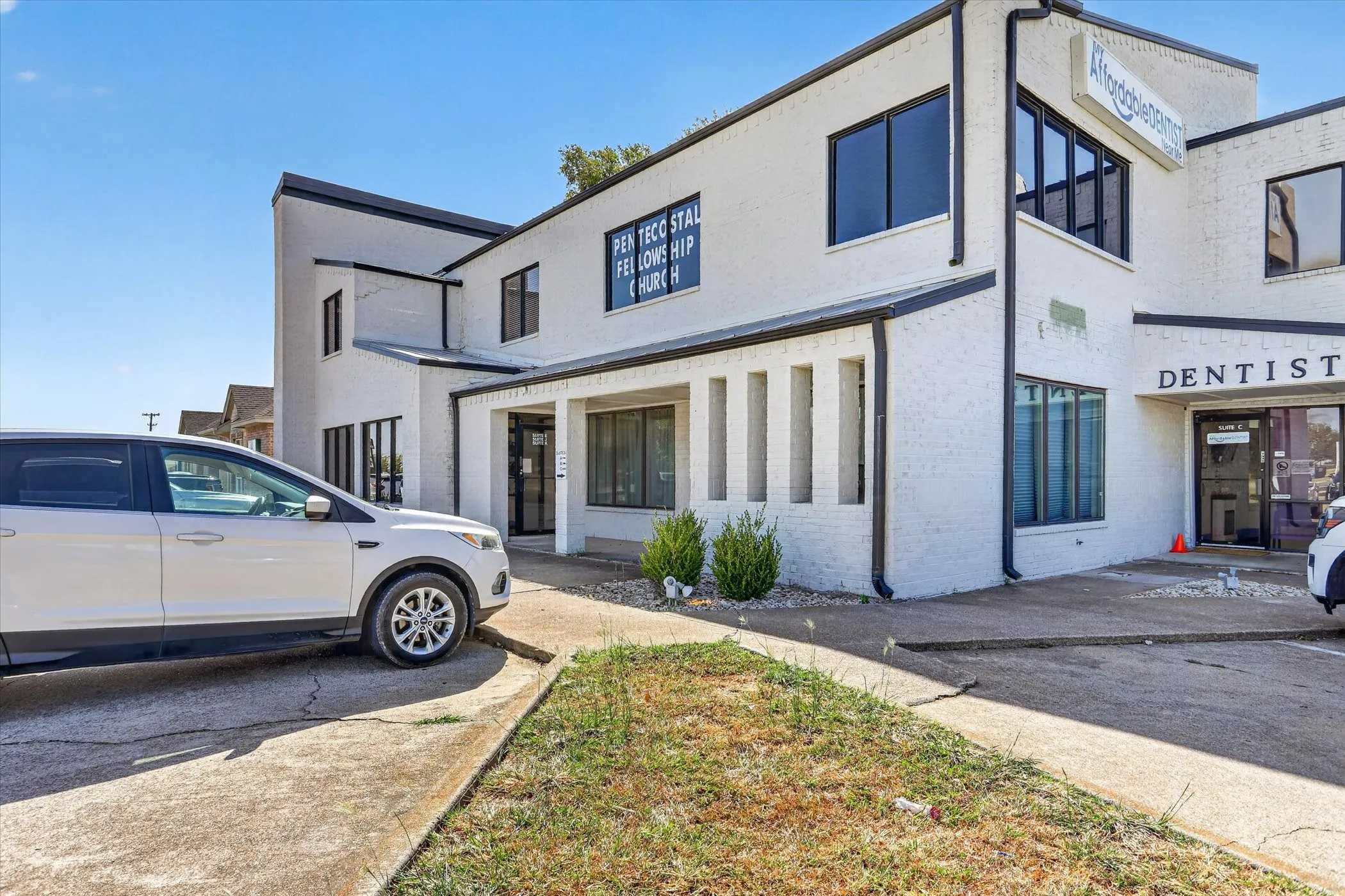 White brick exterior with black trim, multiple large windows, and a concrete parking area