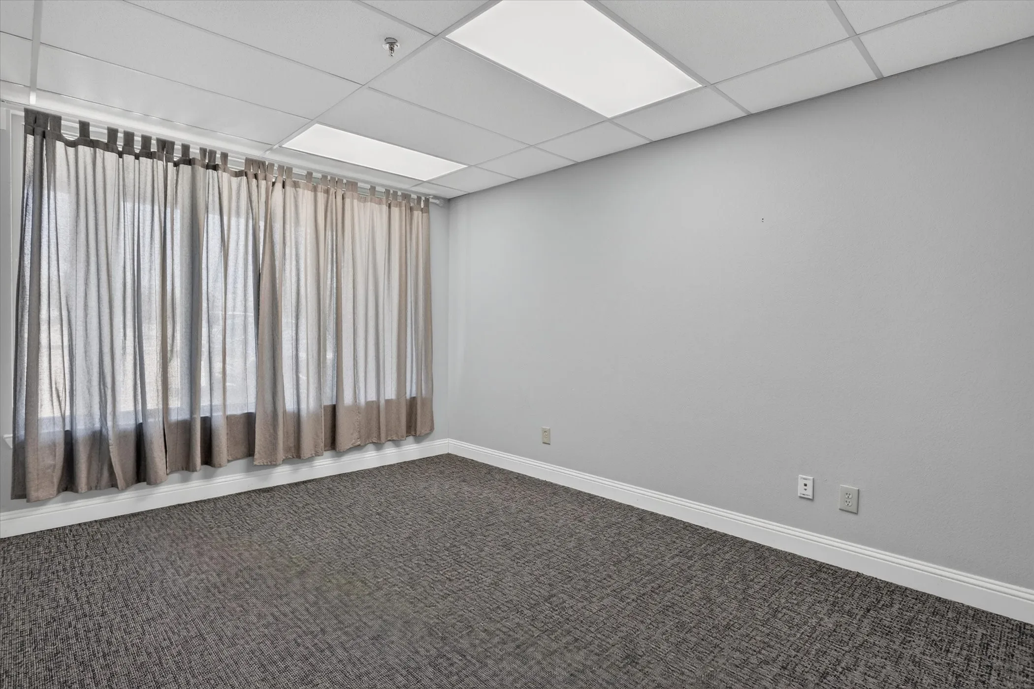Wall-to-wall carpeting, window with drapery, neutral wall paint, and suspended ceiling with recessed lighting