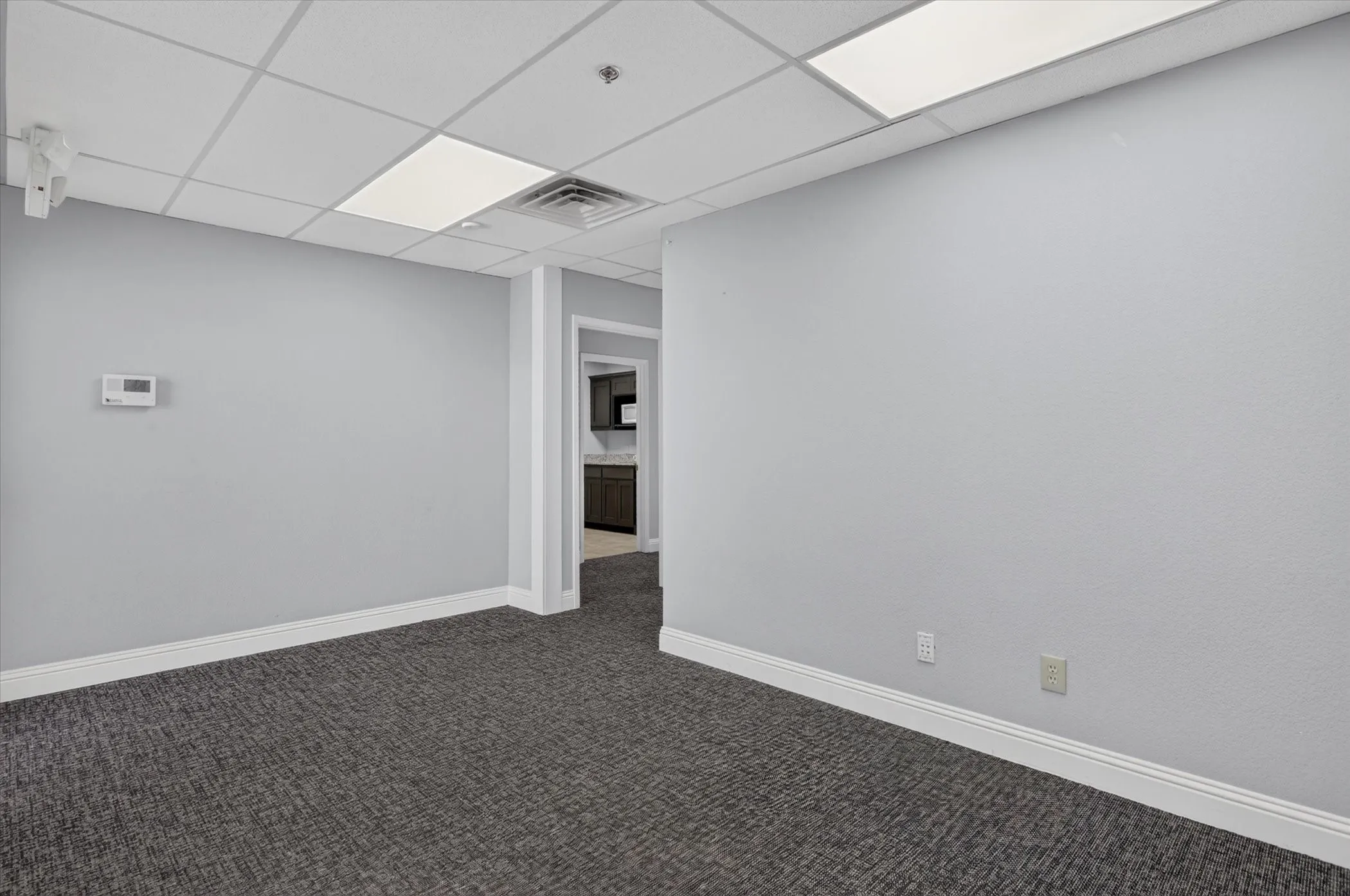 Drop ceiling with integrated fluorescent lighting, textured gray walls, and gray patterned carpeting