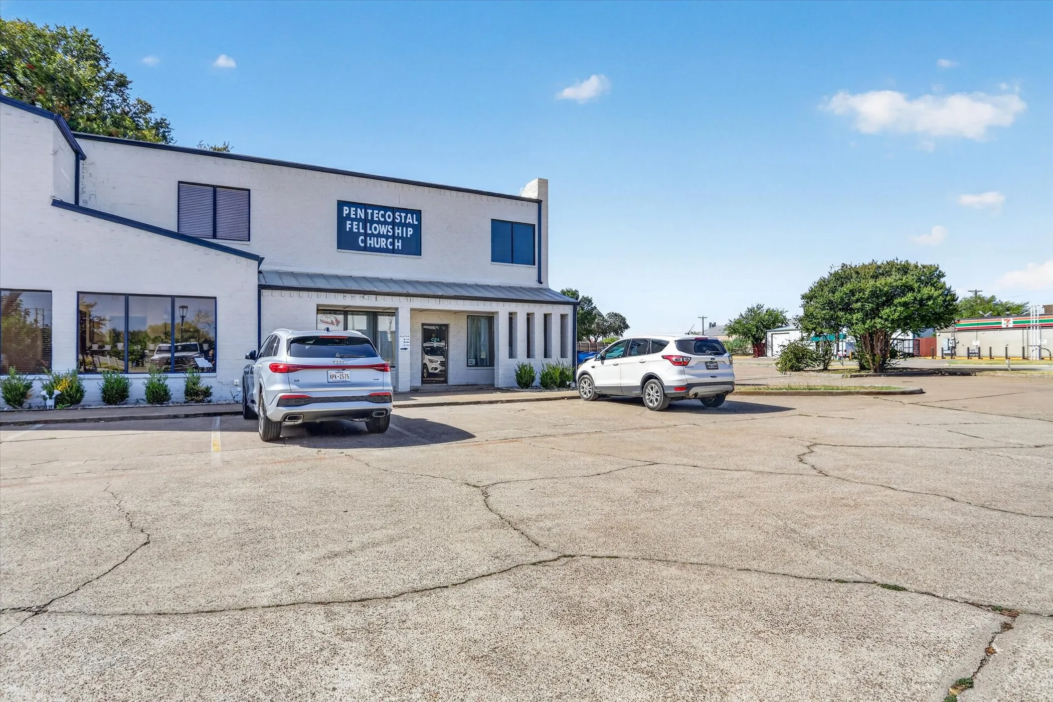 Two-story commercial building with a white exterior, multiple large windows, and a paved parking area