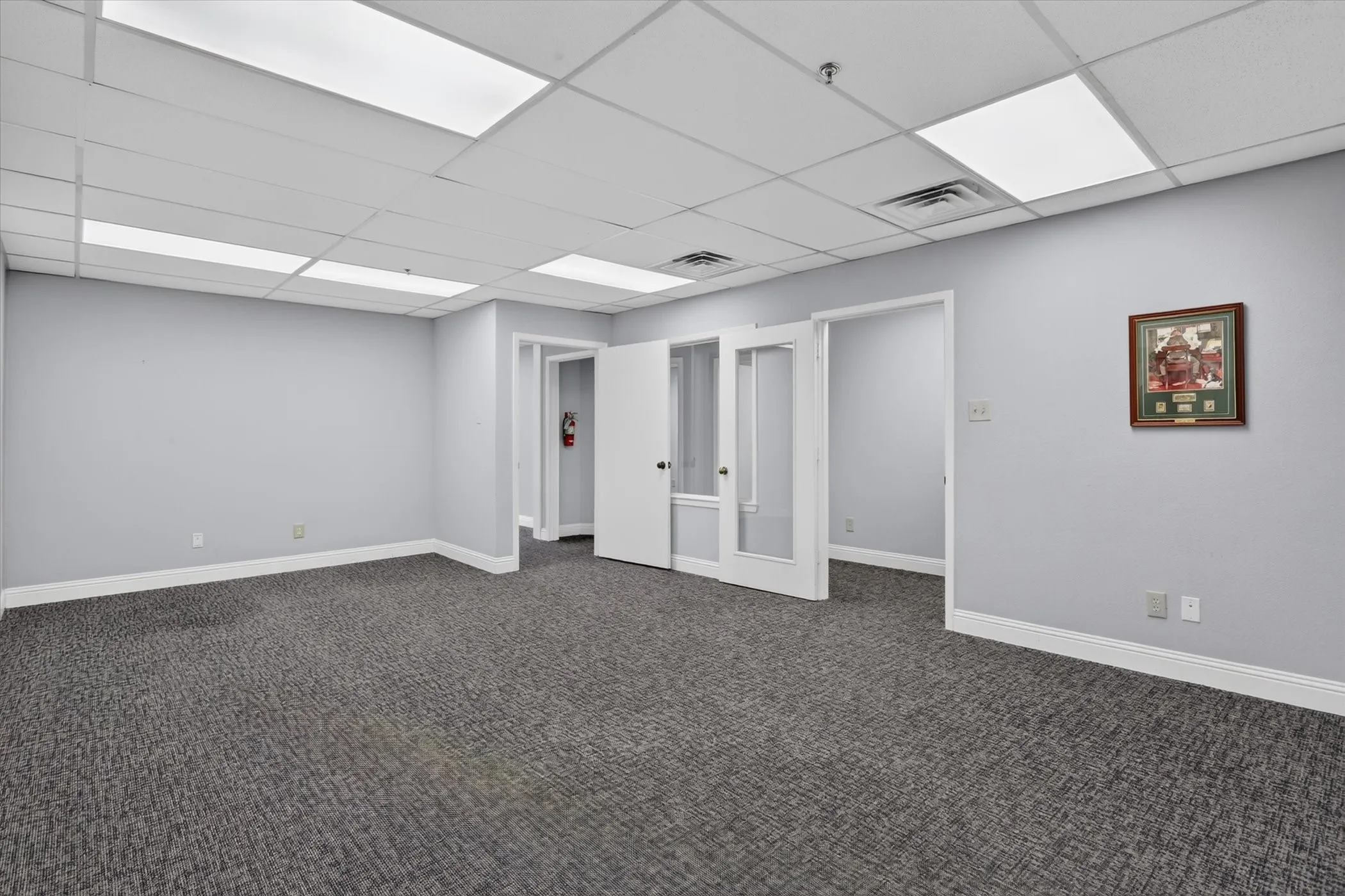 Recessed grid ceiling with integrated lighting, carpet flooring, light gray wall finish, and white interior doors with frosted glass panels