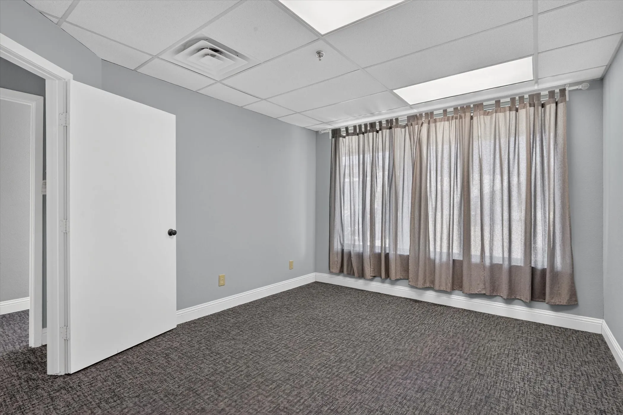 Wall-to-wall carpeting, suspended ceiling, recessed lighting, and window with drapes