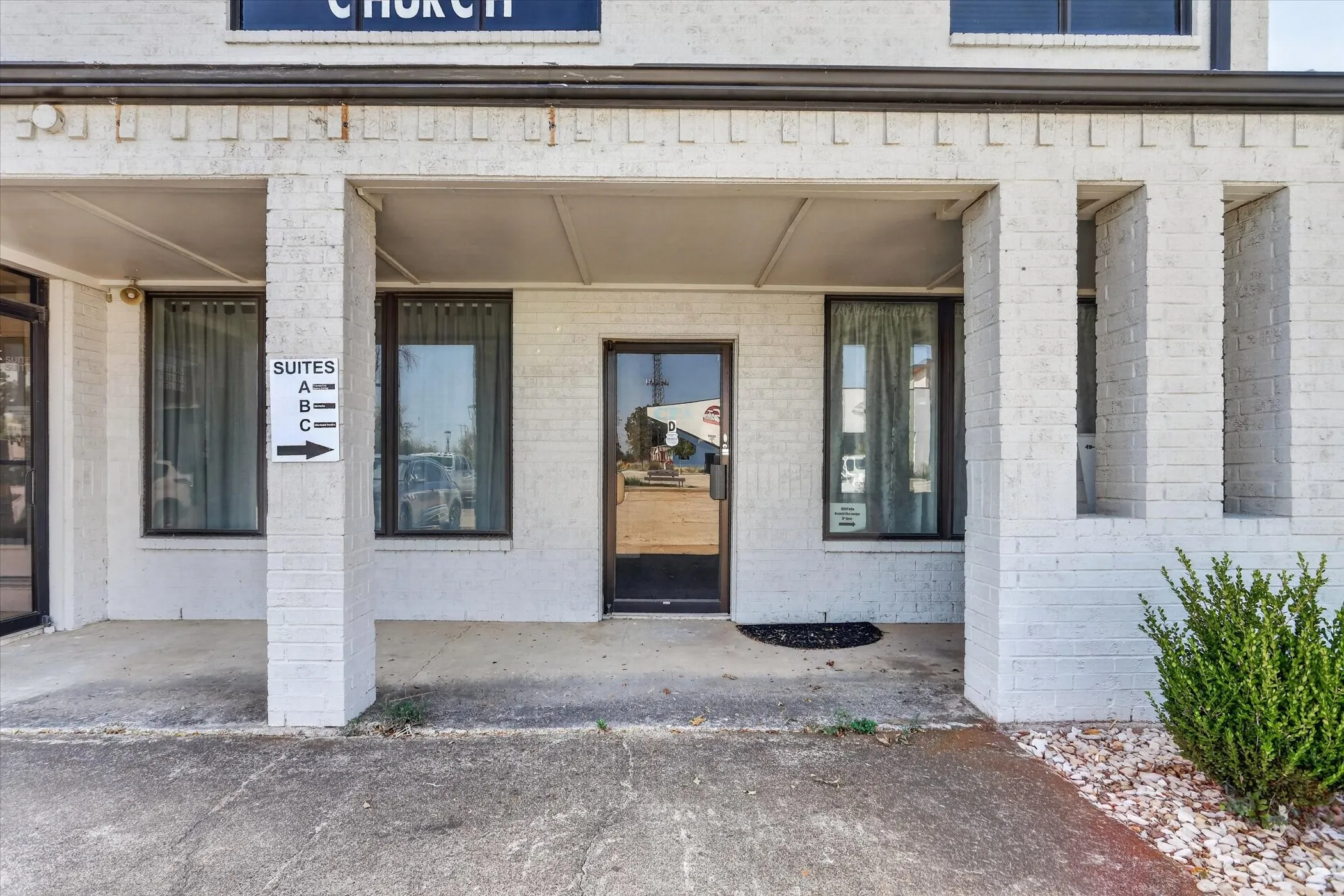 White brick exterior with covered entry, multiple windows, and a glass-paneled entry door