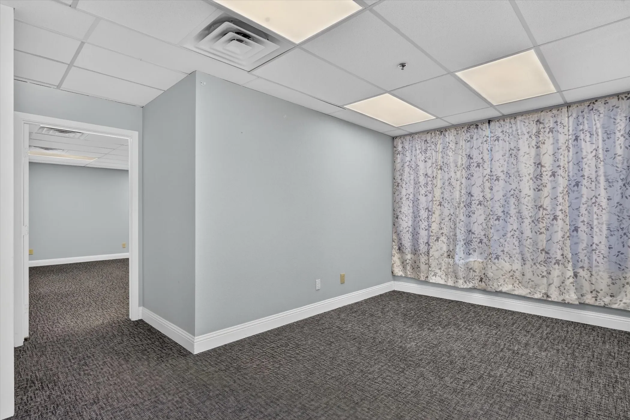 Textured carpet flooring, light gray wall paint, white trim, drop ceiling with recessed lighting, and a patterned curtain
