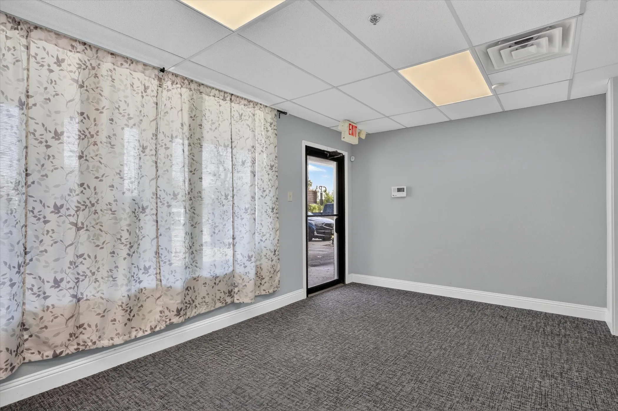 Textured gray carpeting, light gray wall paint, suspended acoustic tile ceiling, recessed lighting, and a glass-paneled entry door