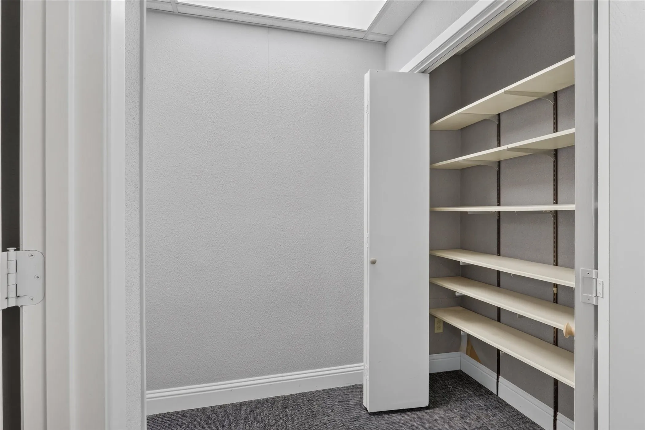 Built-in storage closet with adjustable shelving, white trim, and gray wall texture