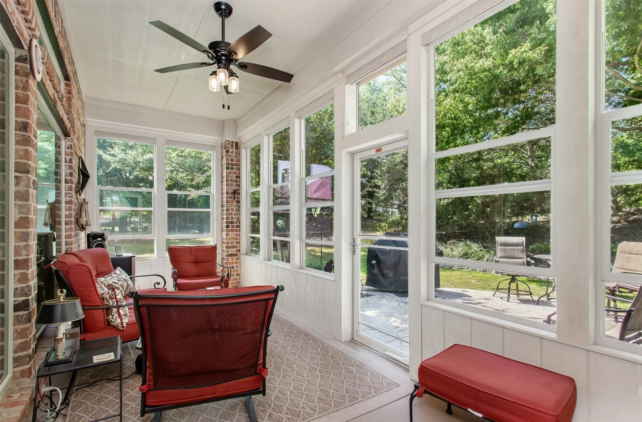 Screened porch with extensive window panels, brick wall accents, a ceiling fan with integrated lighting, and direct access to an exterior patio