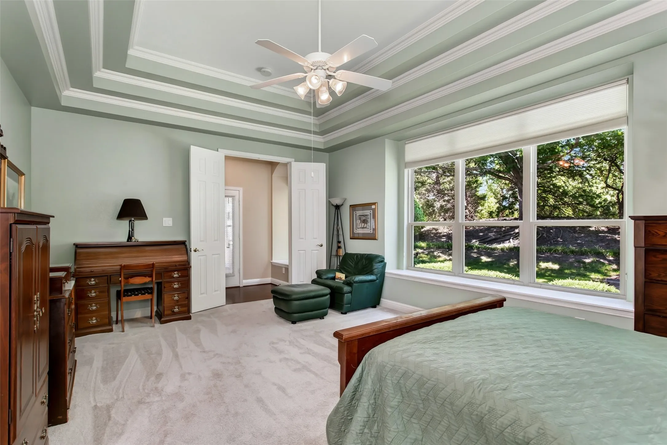 Tray ceiling with decorative molding, large multi-pane window, light-toned carpet, recessed lighting, and ceiling fan