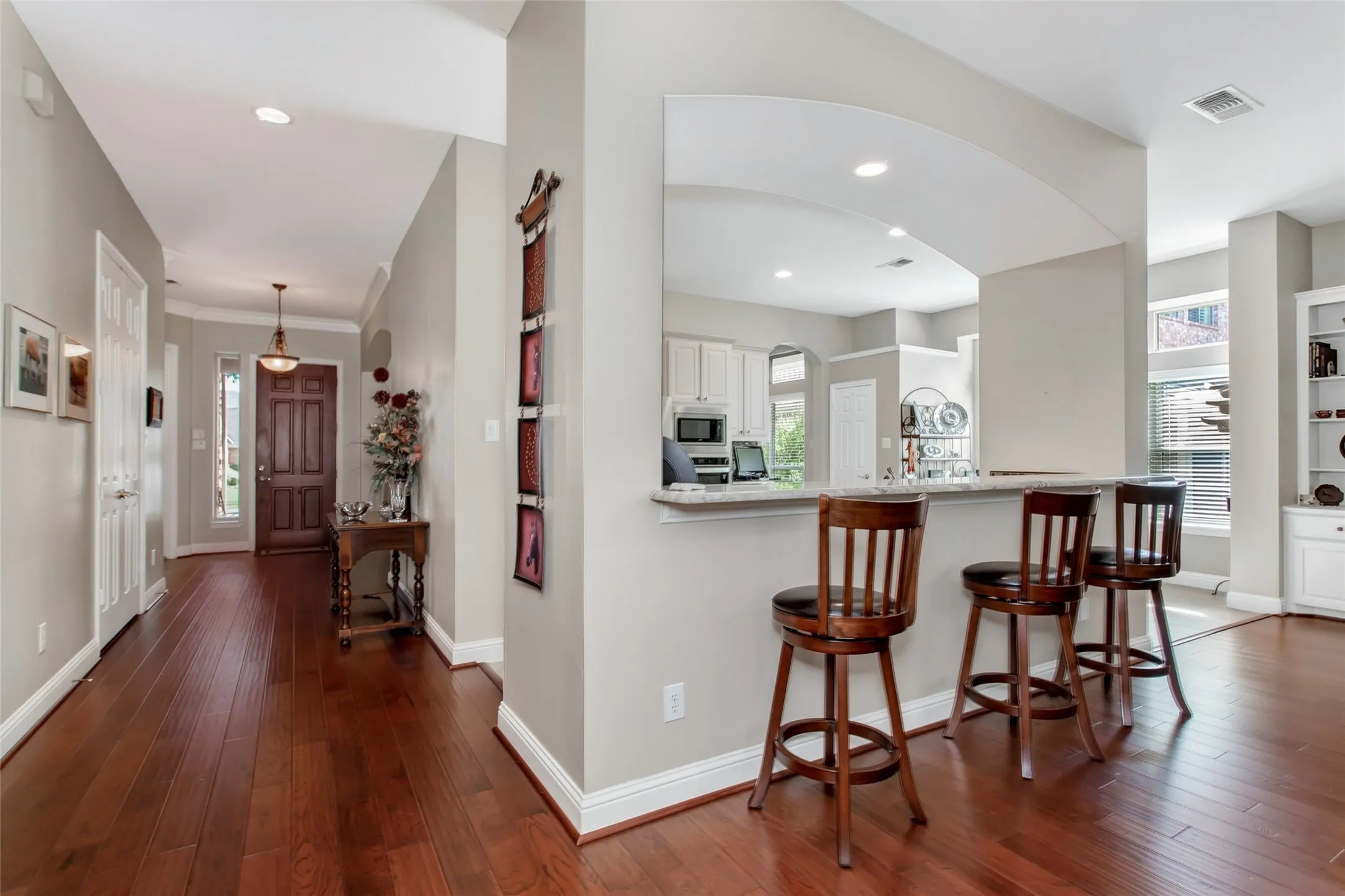 Wood-finish flooring throughout, arched kitchen pass-through, recessed lighting, and a paneled entry door with sidelight