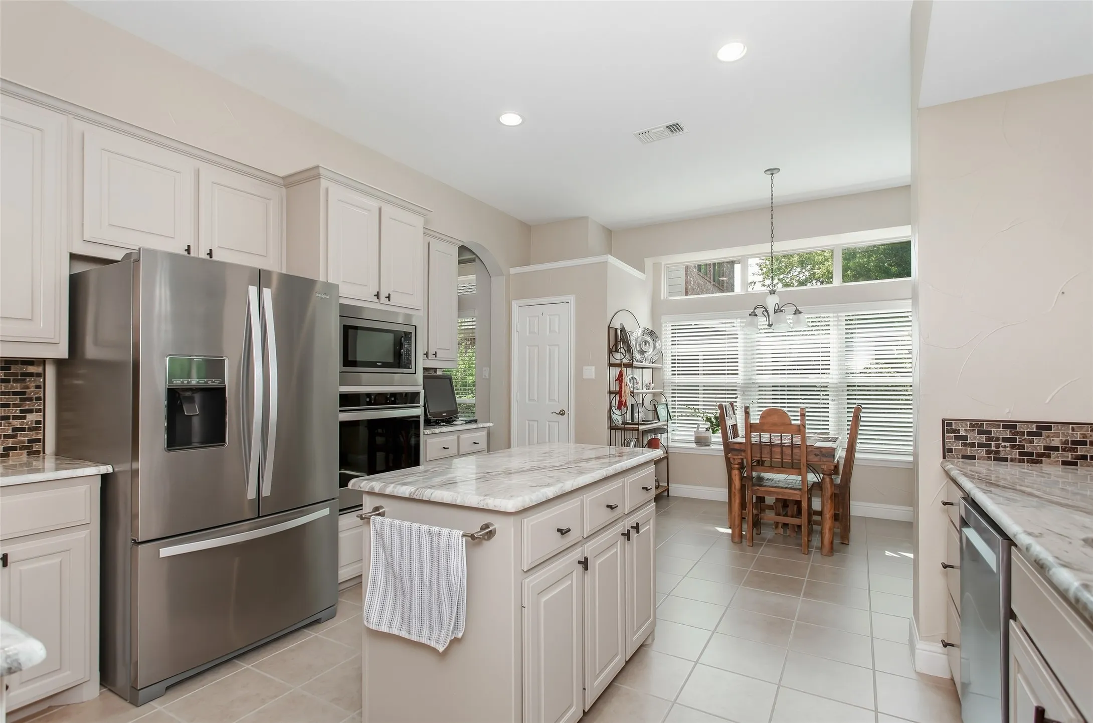 Kitchen featuring light-colored cabinetry, stainless steel appliances, a center island with countertop, tile flooring, and a dining area with expansive windows