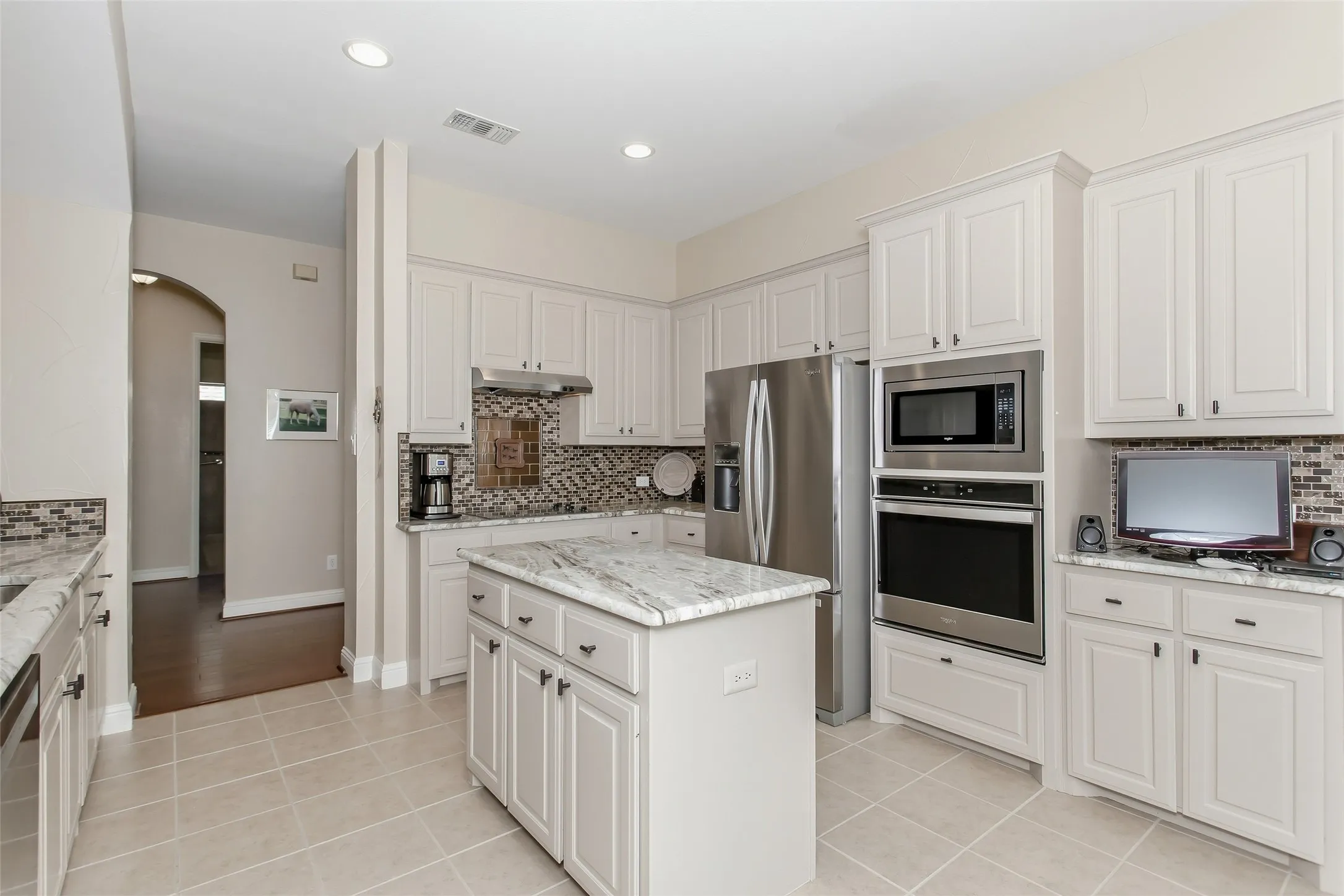 Kitchen featuring a center island with light-toned countertop, white cabinetry with dark hardware, recessed lighting, and stainless steel appliances including a built-in oven and microwave