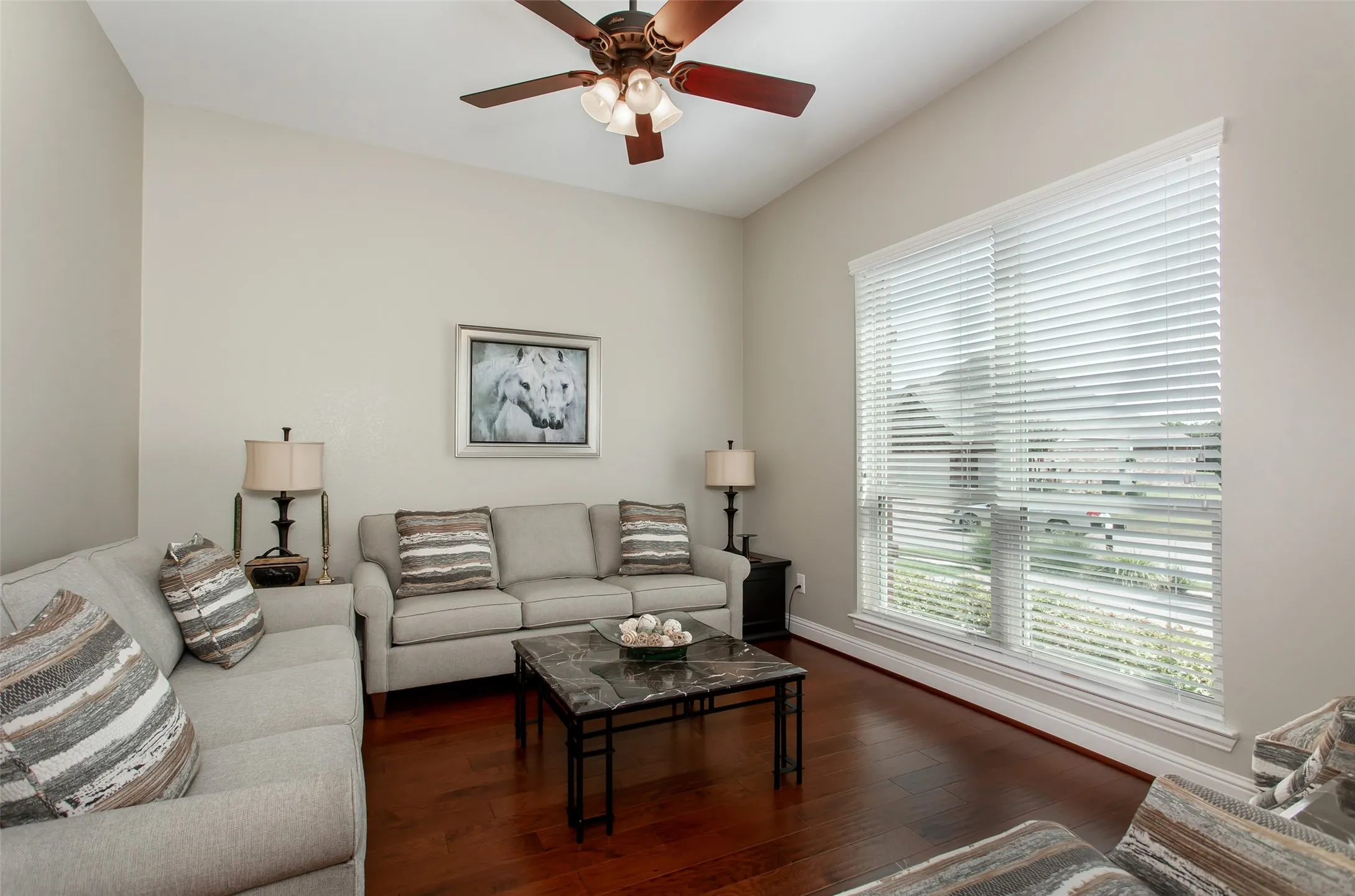 Vaulted ceiling with a ceiling fan, large window with blinds, wood-finish flooring, and light-toned wall paint