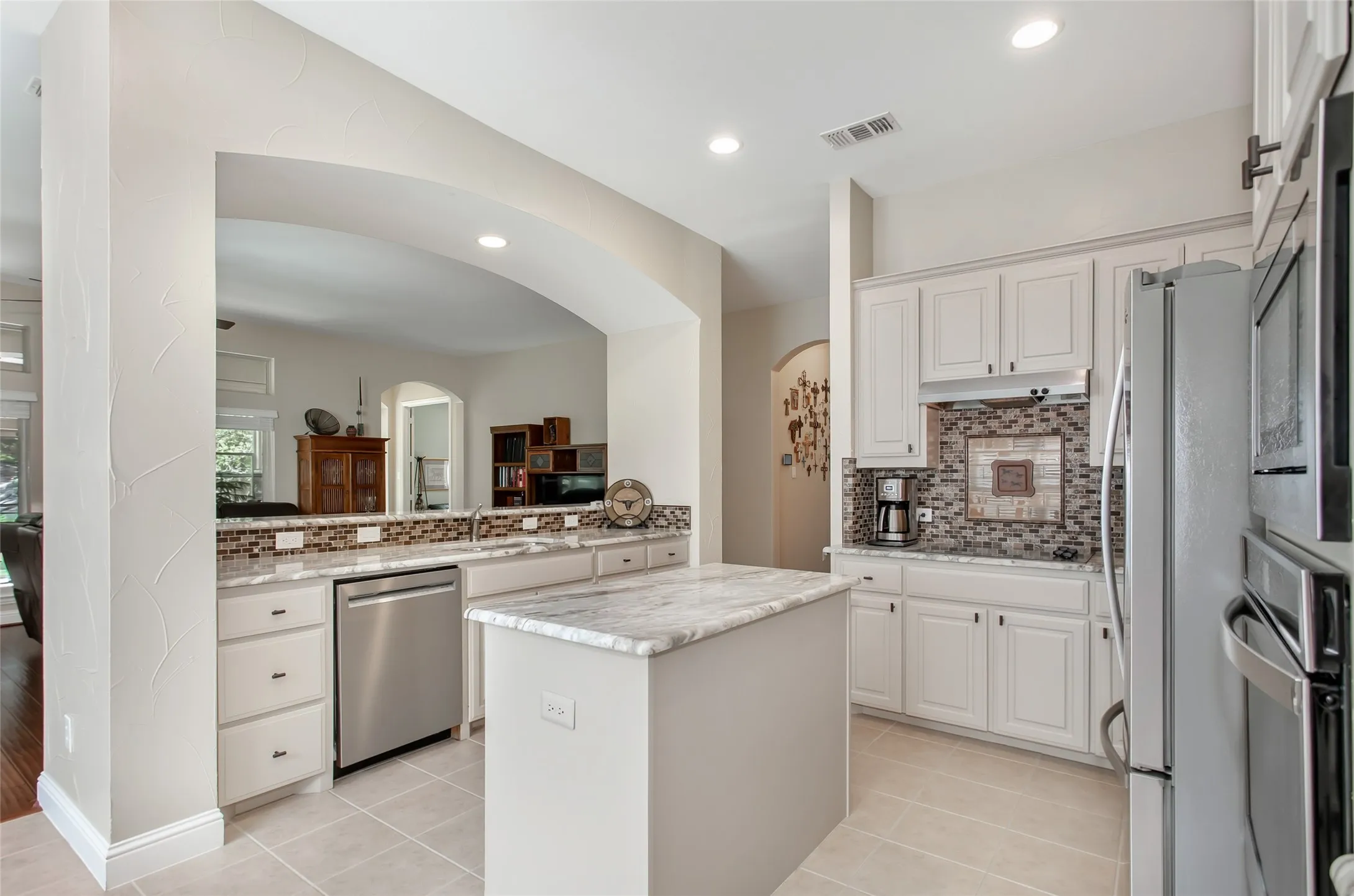 Kitchen featuring white cabinetry, light-toned countertops, a mosaic tile backsplash, stainless steel appliances, and recessed lighting