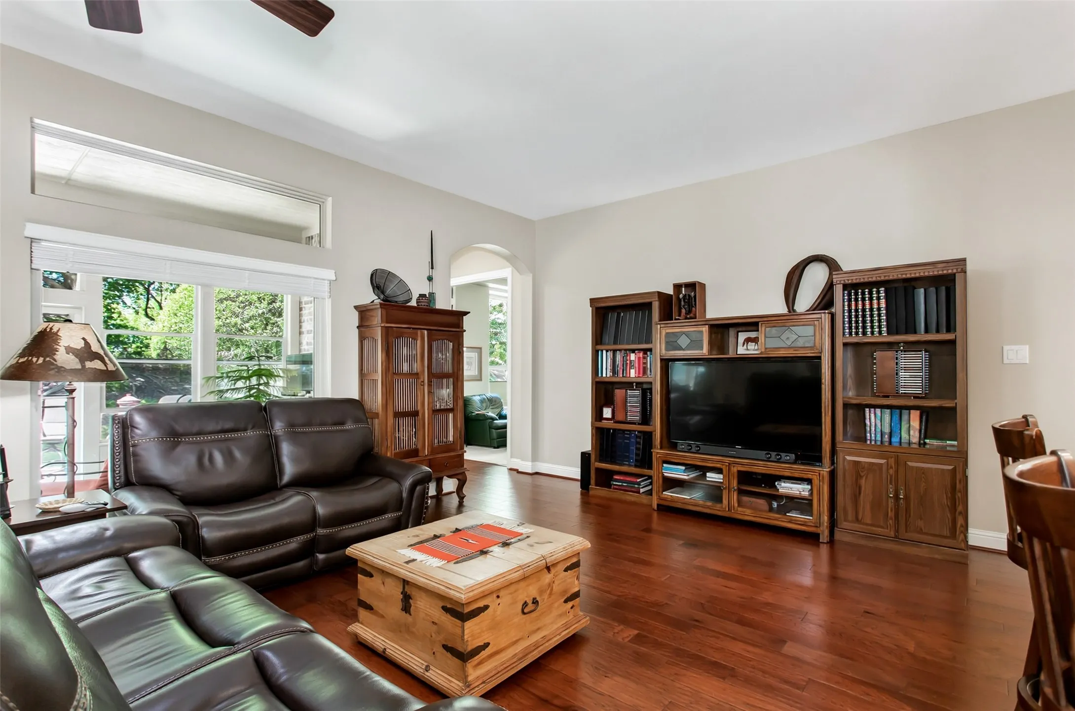 Wood-finish flooring, high ceilings, large windows with upper transom windows, ceiling fan, and arched doorway