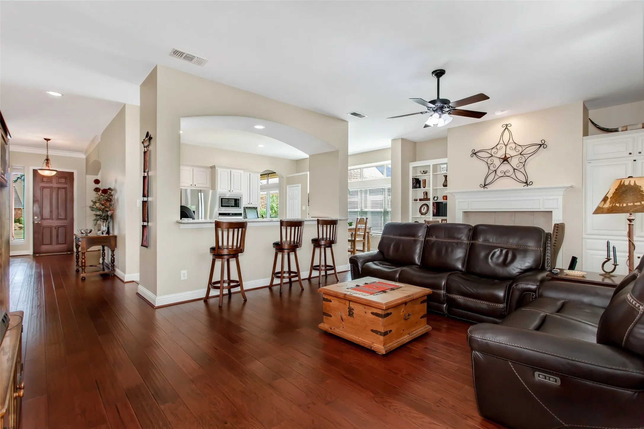 Hardwood-finish flooring throughout, fireplace with mantle, built-in shelving, ceiling fan, and arched pass-through to the kitchen